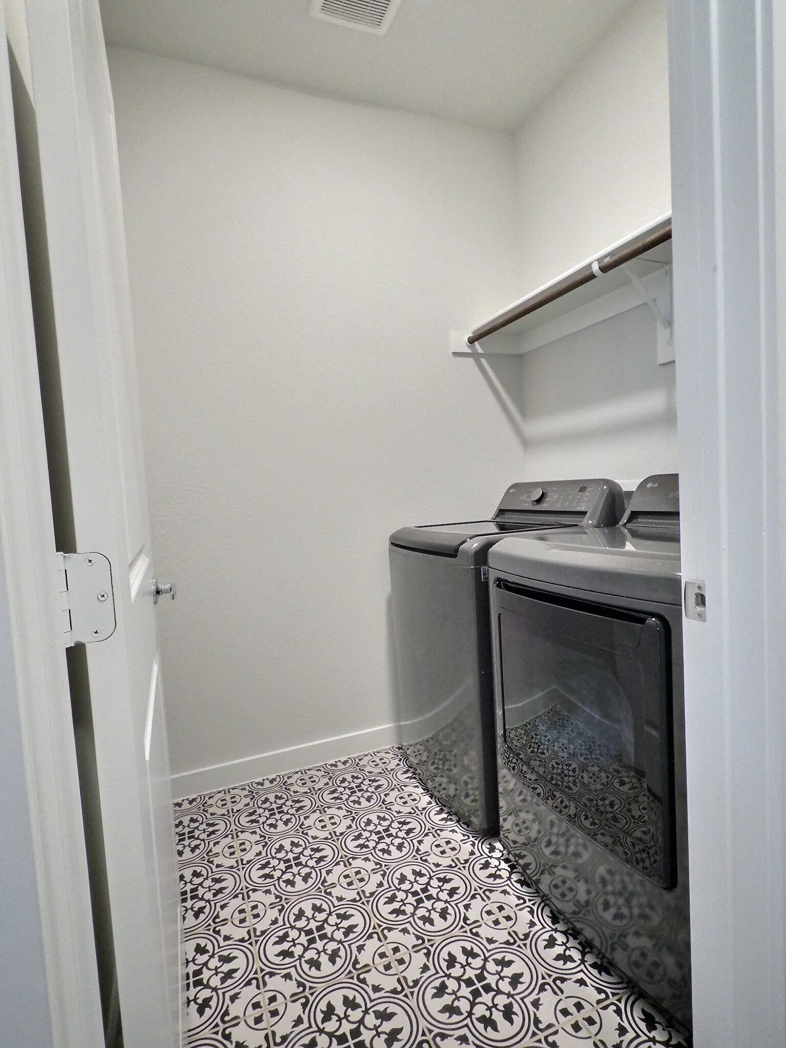 This utility room features patterned floor tiling, a white wall shelf, and space for appliances