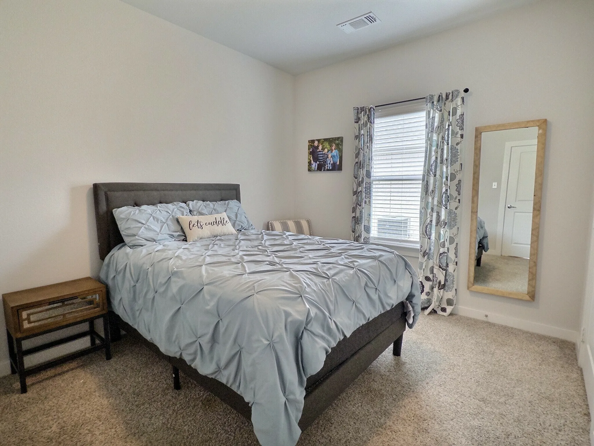 This room features light-colored walls and carpeting, a window with blinds, and curtains