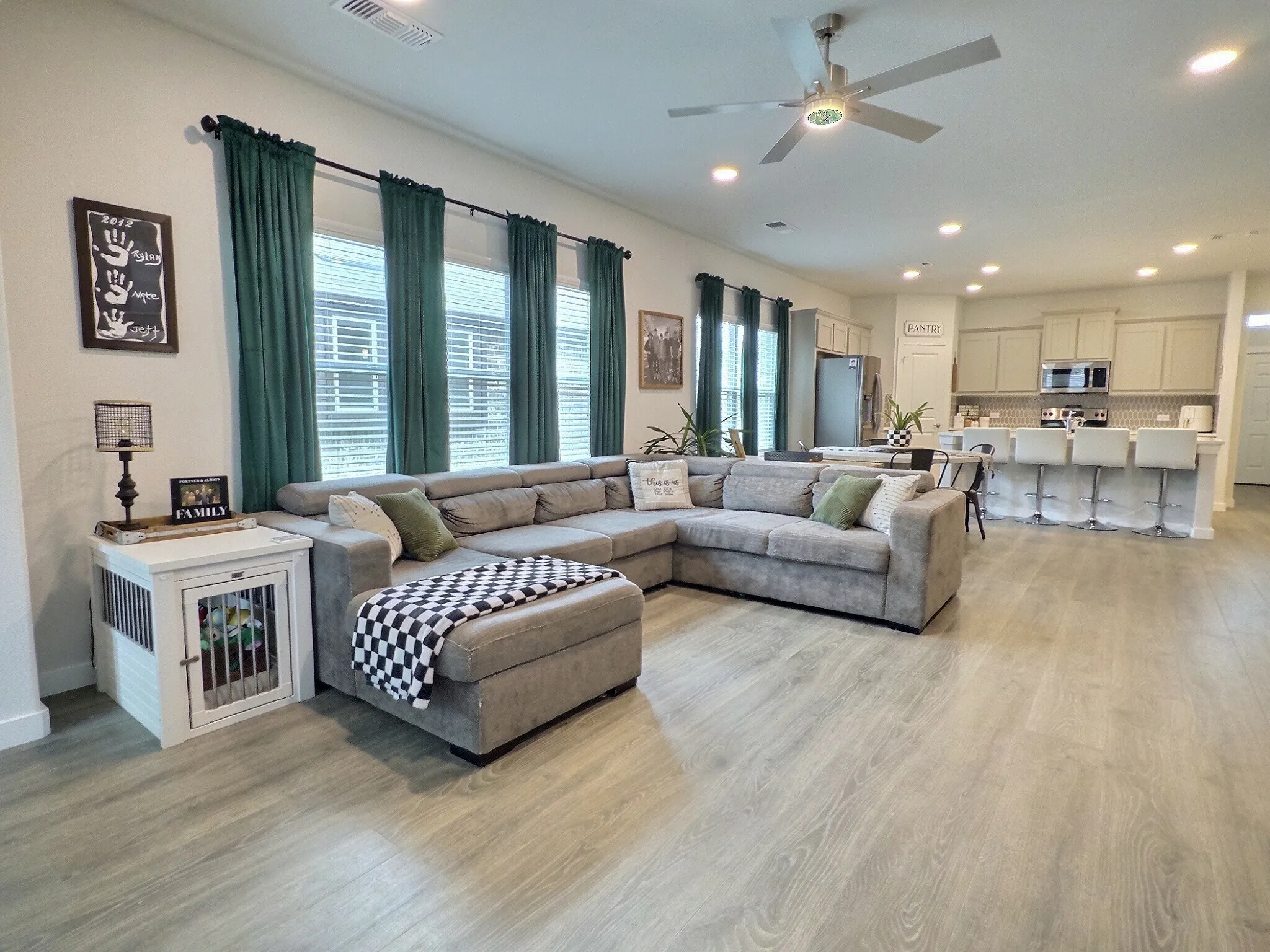 Open concept living area featuring light-toned flooring, a ceiling fan with integrated lighting, and multiple windows with blinds