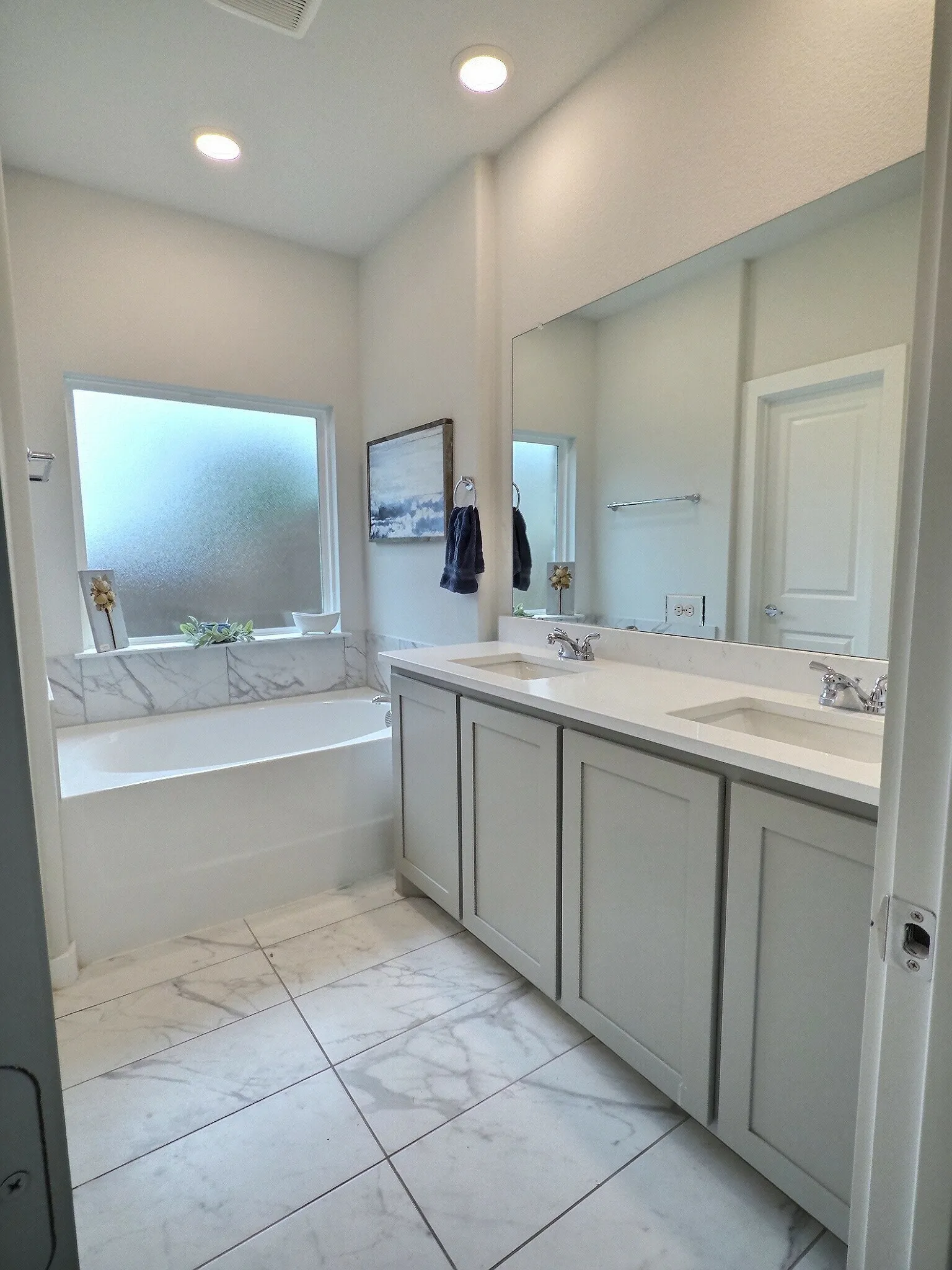 The bathroom features a double vanity with light-colored cabinetry and integrated sinks, complemented by an expansive mirror