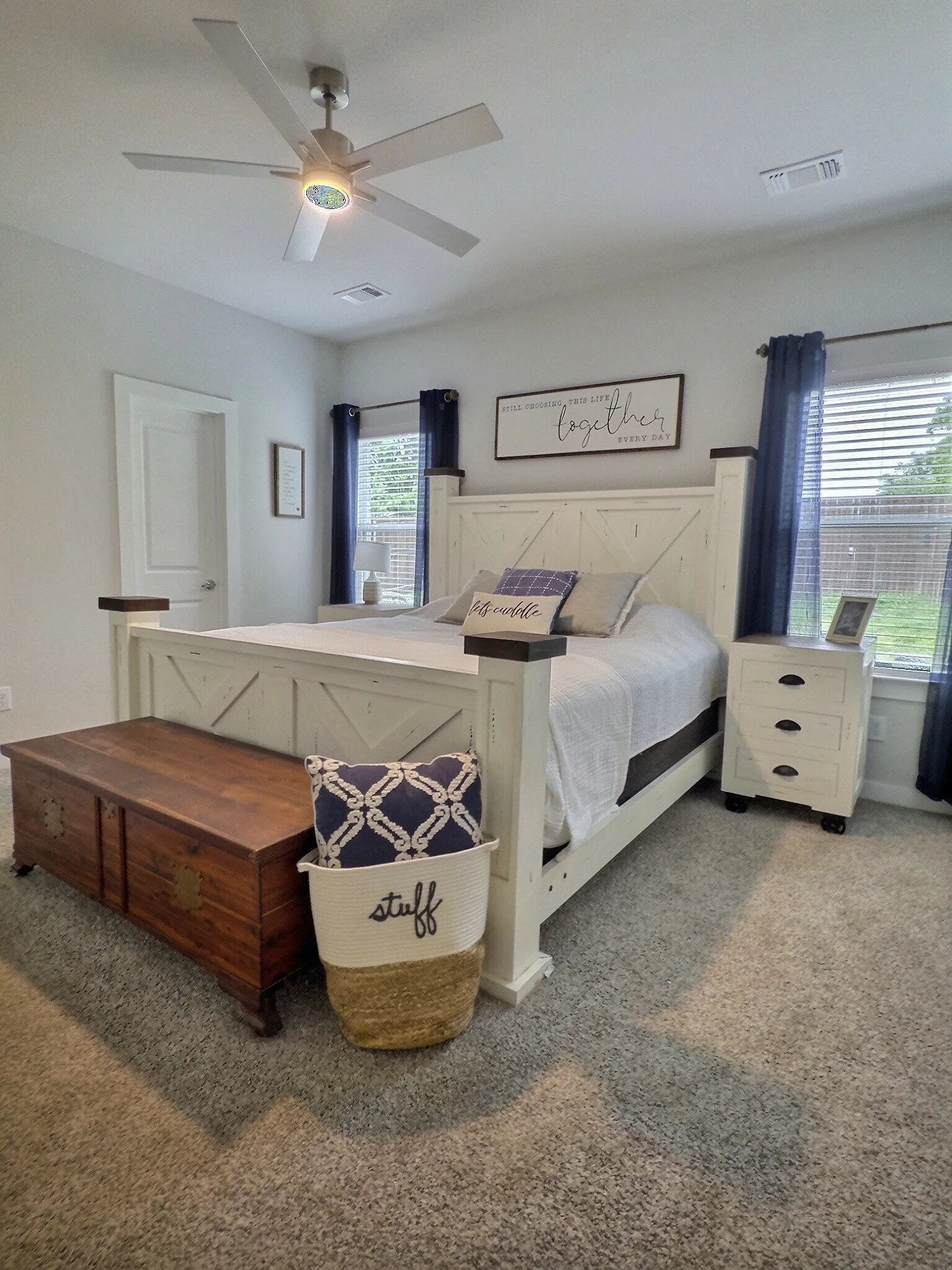 This bedroom features soft carpeting, a ceiling fan with integrated lighting, and windows with blinds providing natural light