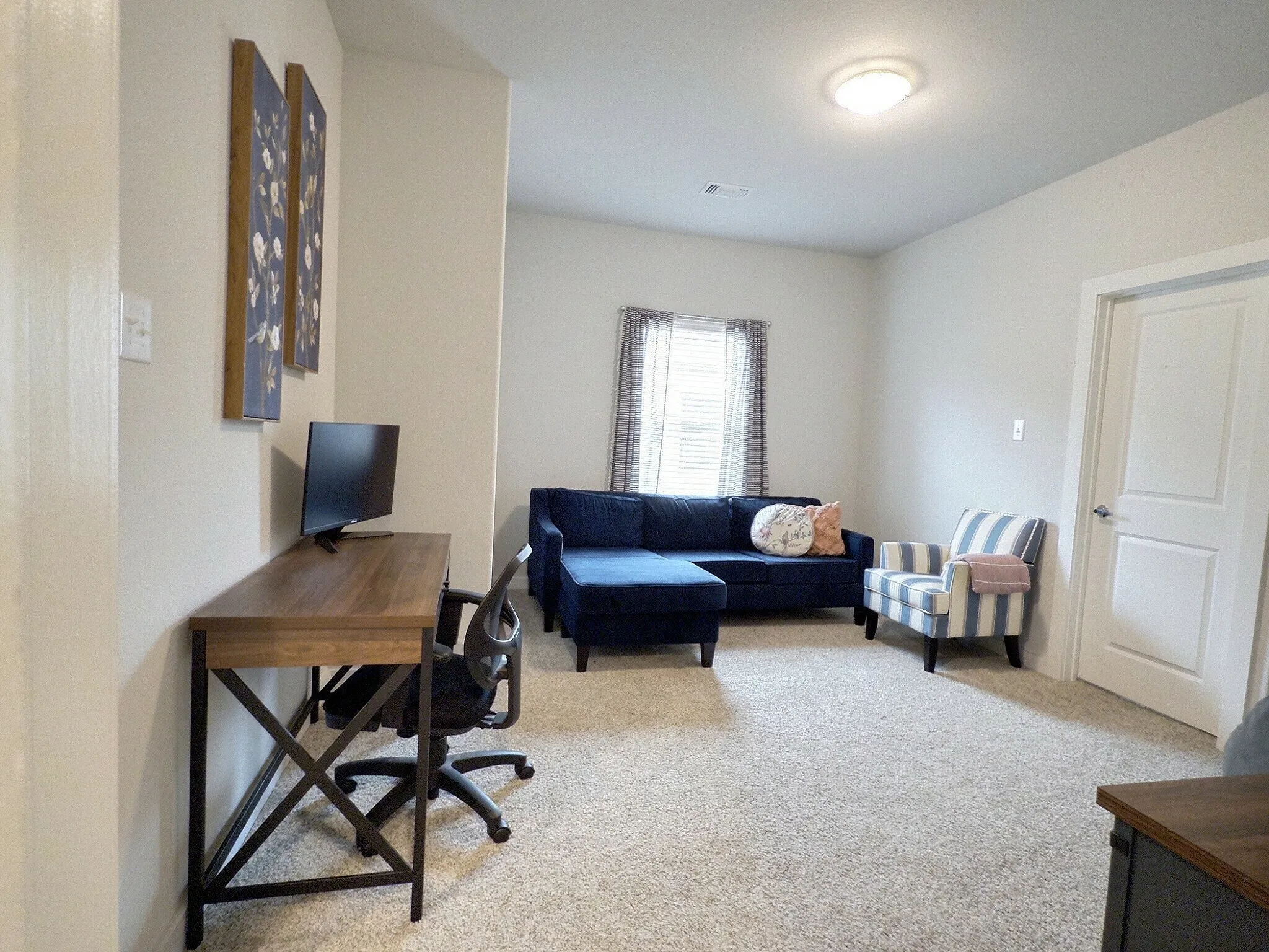 This versatile room features neutral-toned carpet, light-colored walls, and a window with blinds providing natural light