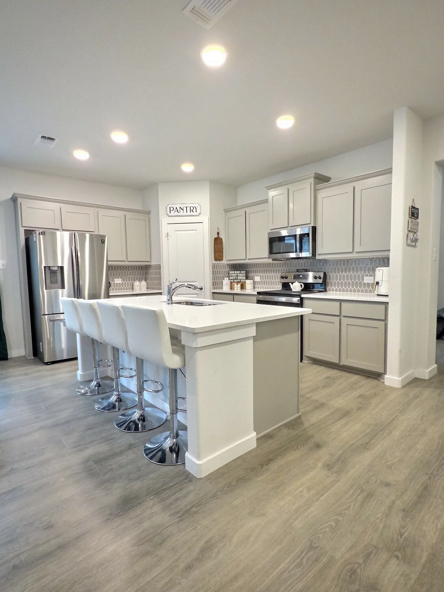 Modern kitchen featuring an island with a white countertop and seating, stainless steel appliances, and grey cabinetry