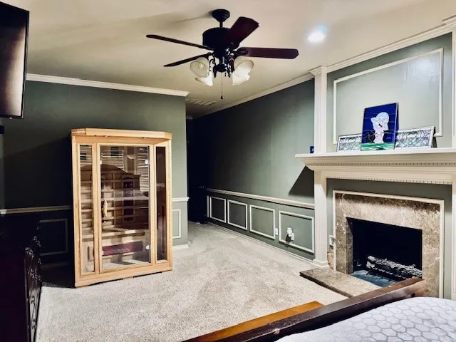 Carpeted bedroom featuring crown molding, a decorative wall, ceiling fan, a fireplace with raised hearth, and a wainscoted​​‌​​​​‌​​‌‌​‌‌​​​‌‌​‌​‌​‌​​​‌​​ wall