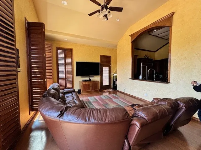 Living area with a textured wall, a ceiling fan, vaulted ceiling, and wood finished floors