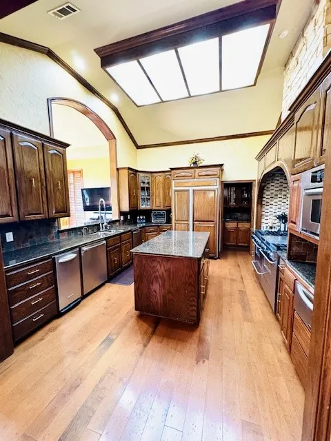Kitchen featuring visible vents, a center island, light wood-style floors, high end appliances, and vaulted ceiling