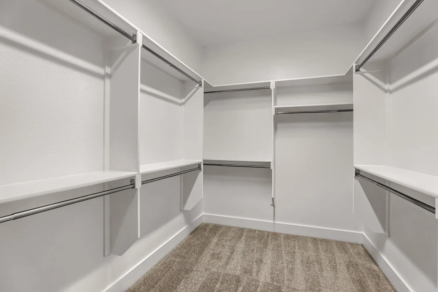 Walk-in closet with integrated shelving, multiple hanging rods, and neutral-toned carpeting
