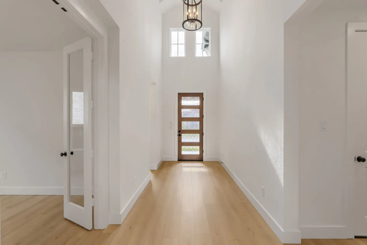Vaulted entry featuring wood-finish flooring, a modern front door with frosted glass panels, and a decorative ceiling light fixture
