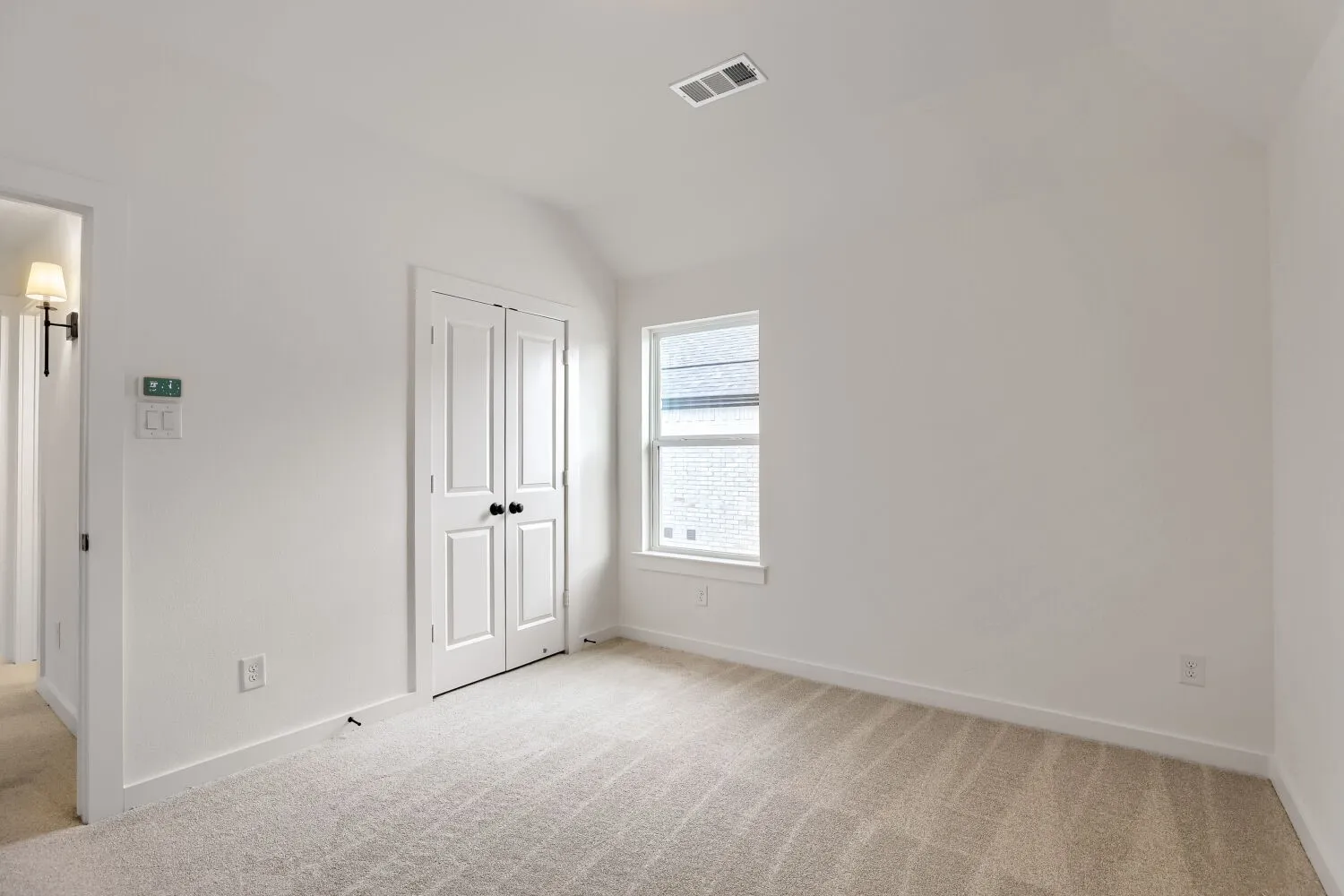 Vaulted ceiling with a flush-mount vent, light-toned carpet, double-pane window, and bifold doors