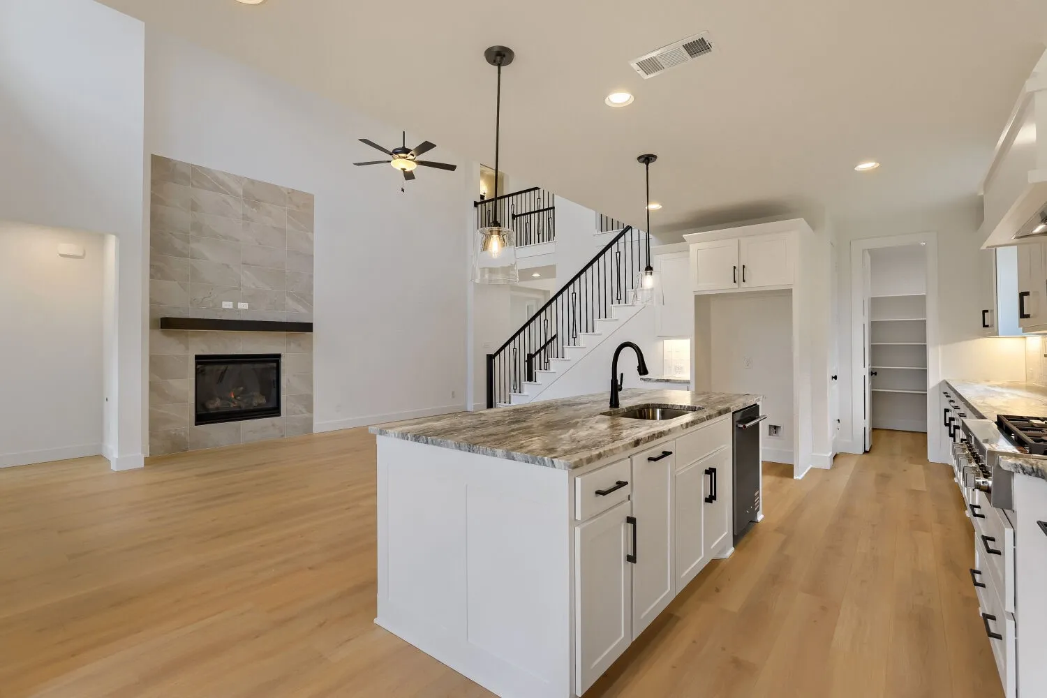 High vaulted ceilings, fireplace with a tile surround and wood mantel, wood-finish flooring, kitchen island with a stone countertop and undermount sink, and white cabinetry