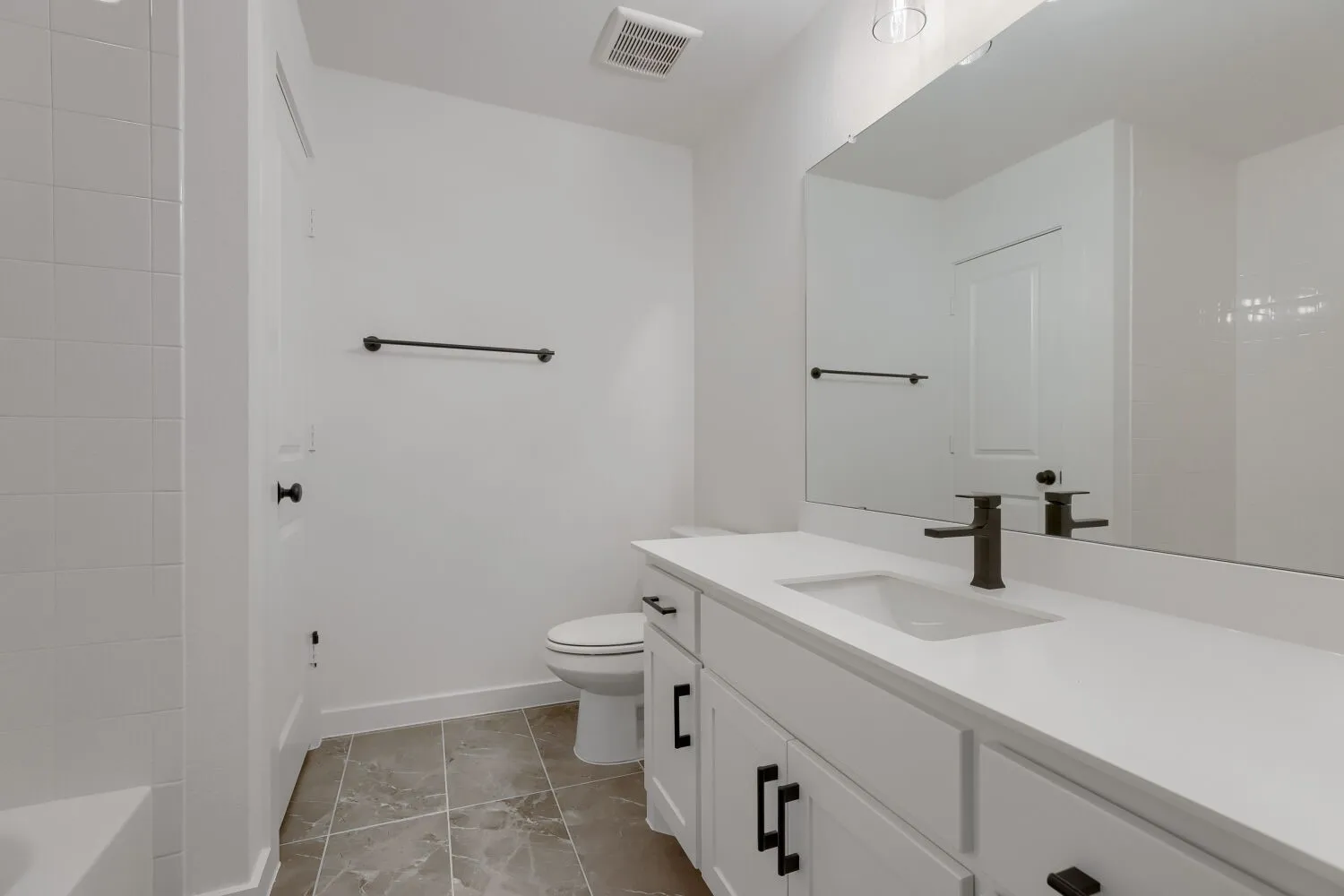 White vanity with black hardware, rectangular undermount sink, bronze-finish faucet, full-width mirror, and gray-toned floor tile