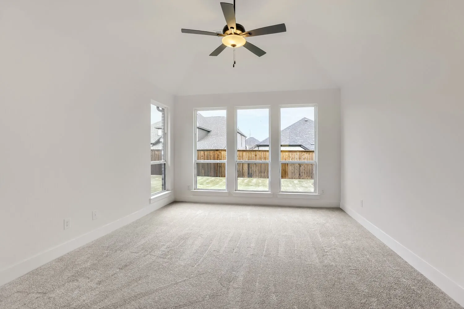 Neutral gray carpeting, vaulted ceiling, and a modern ceiling fan with integrated lighting