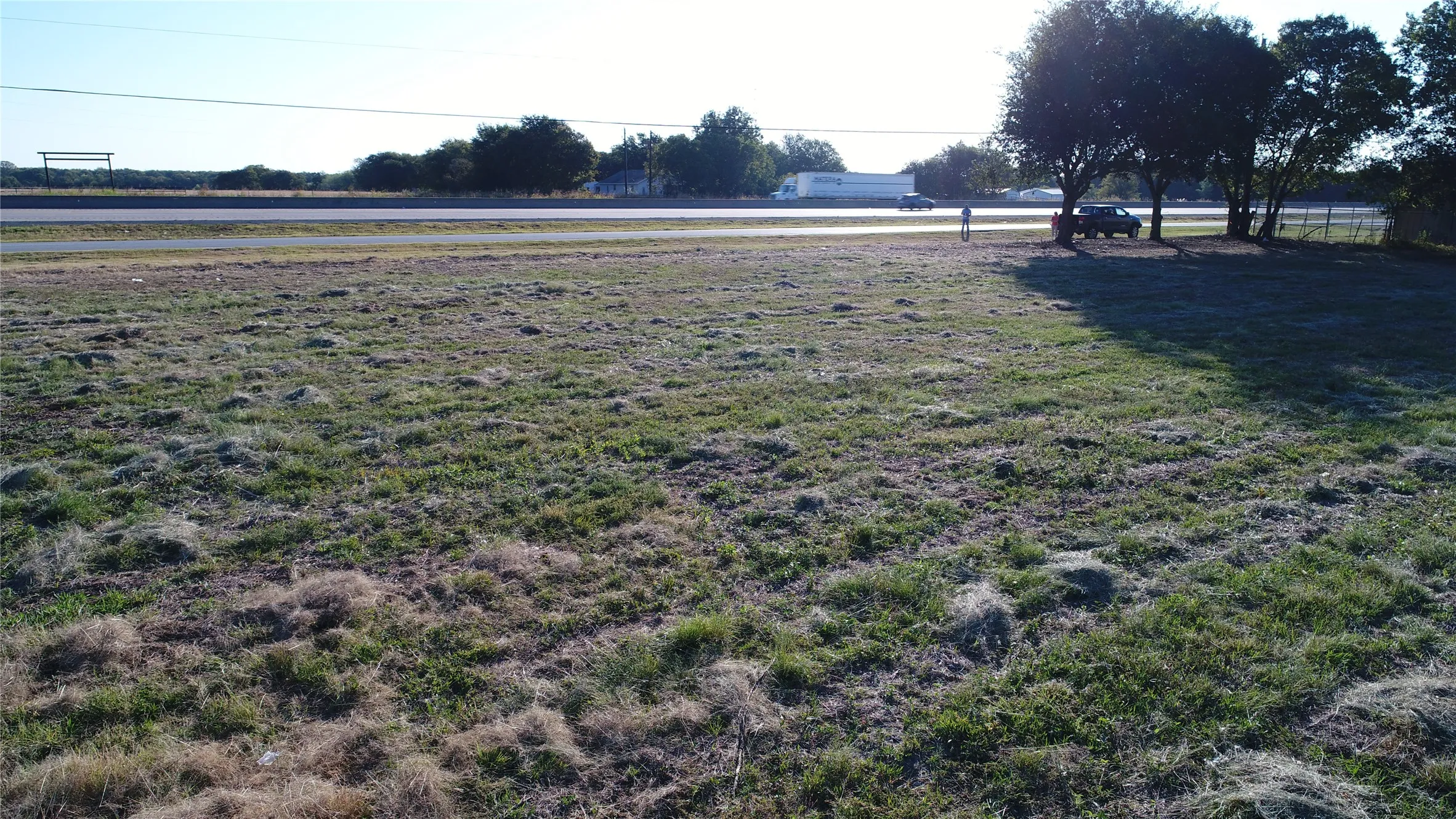 The property features a large grassy area with scattered trees, bordered by a road
