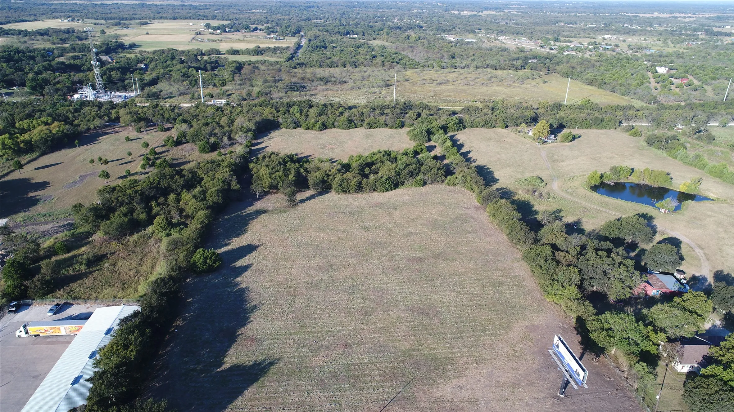 Aerial view showcasing expansive open land, wooded areas, and a visible pond
