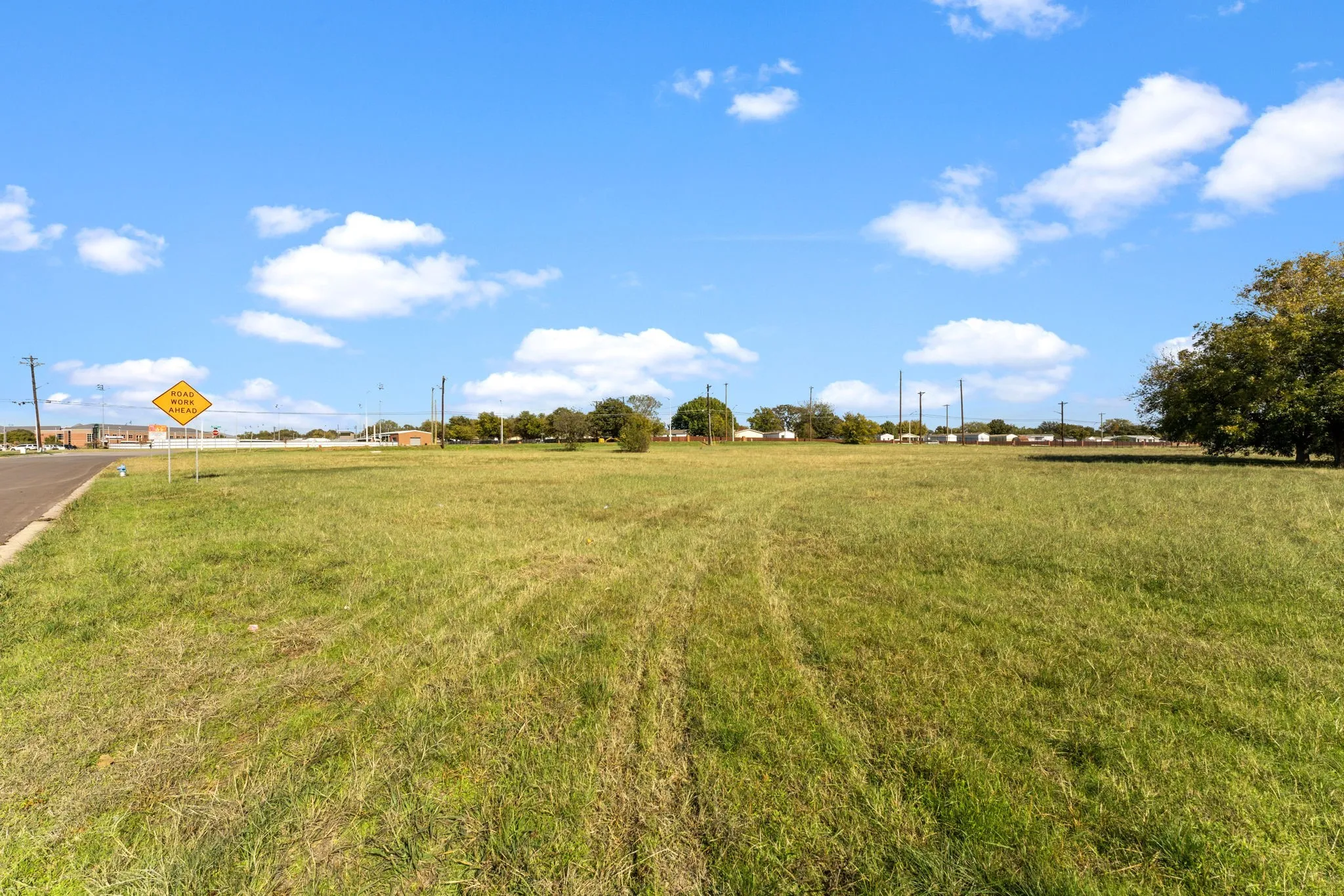 Expansive grassy lot with a clear blue sky, bordered by a paved road