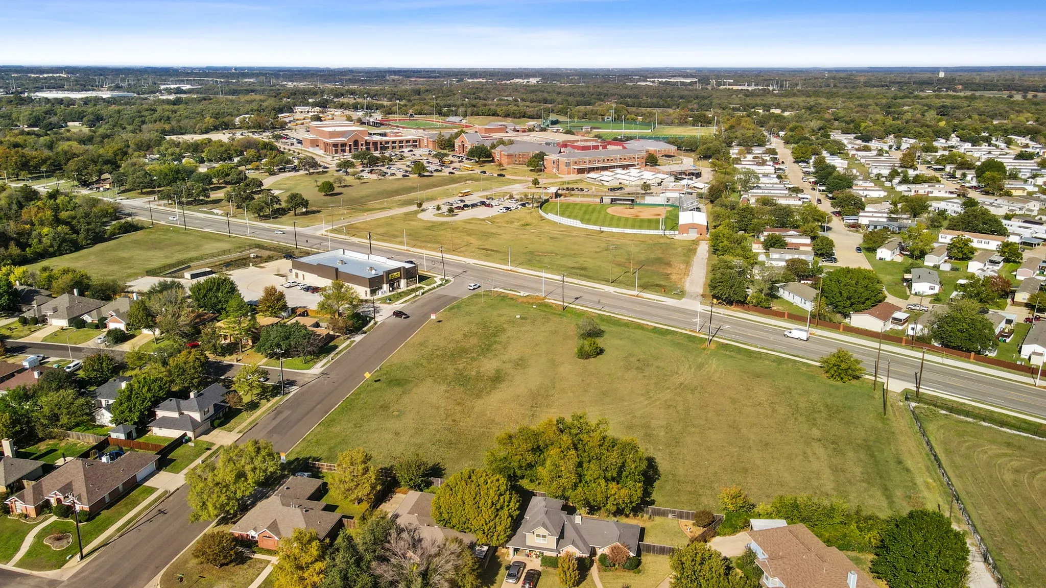Expansive property featuring a large grassy area, surrounded by paved roads and mature trees