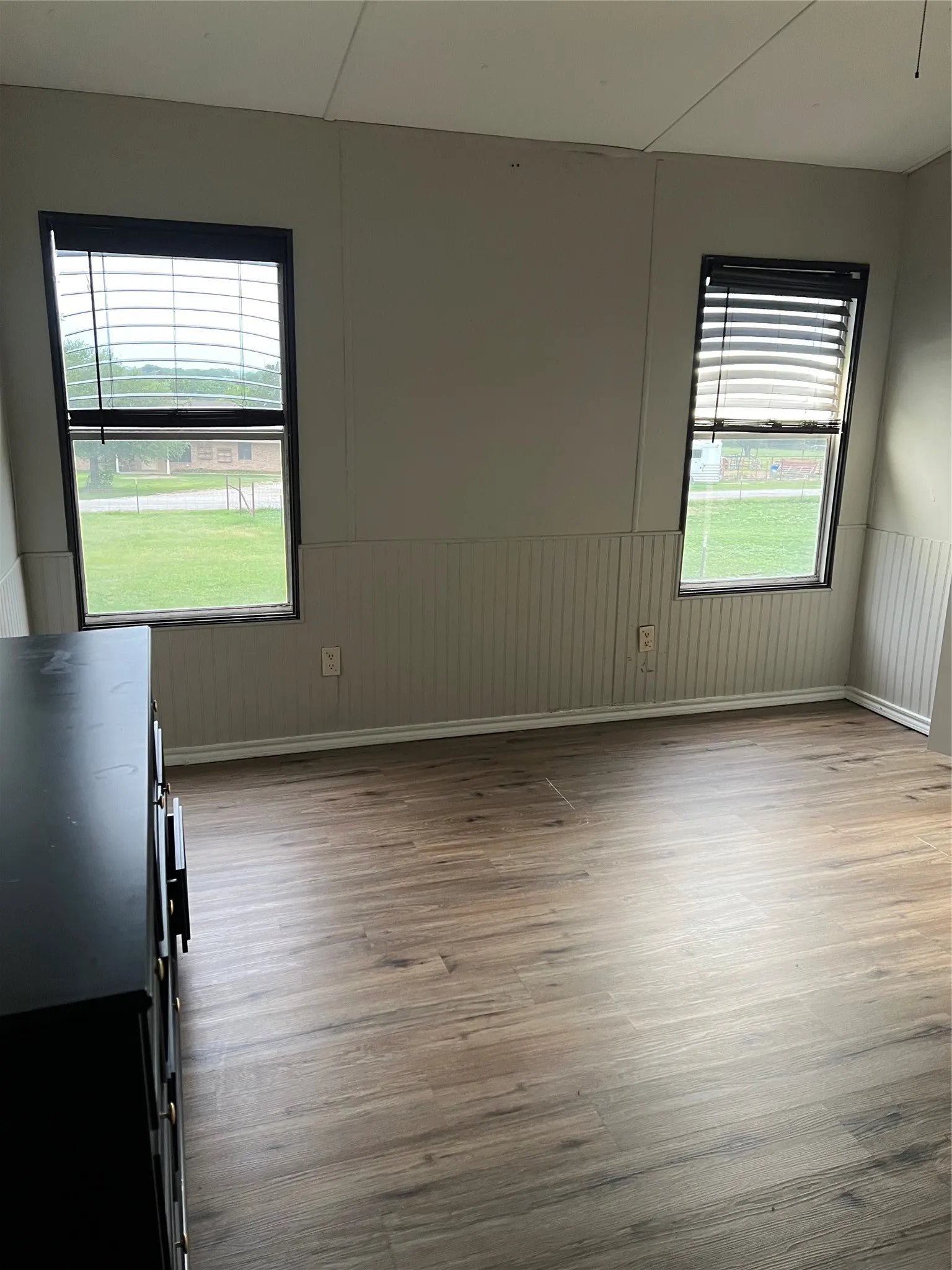 The room features durable wood-look flooring and two windows with blinds
