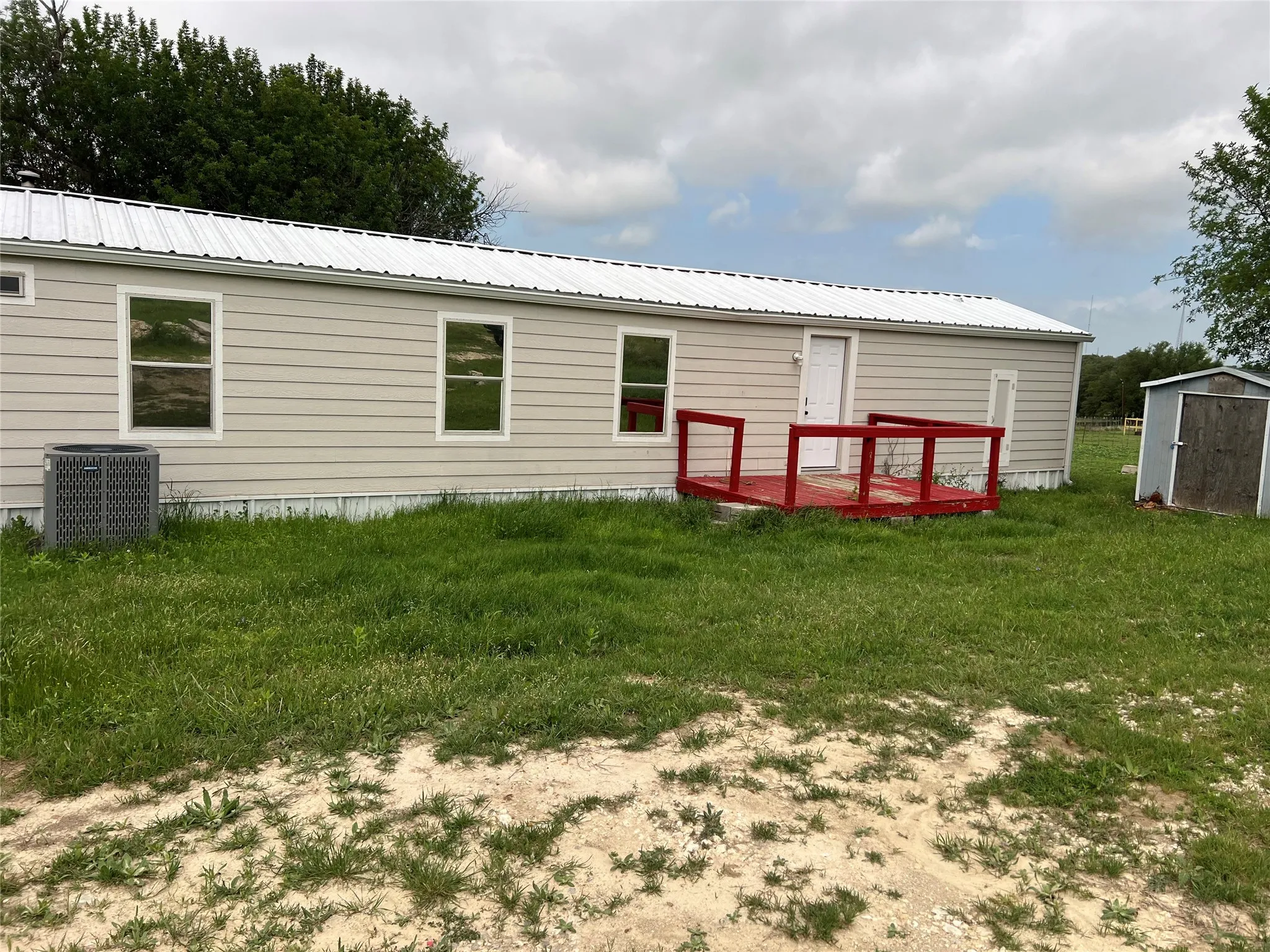 The property features light-colored horizontal siding, a white metal roof, and a red deck