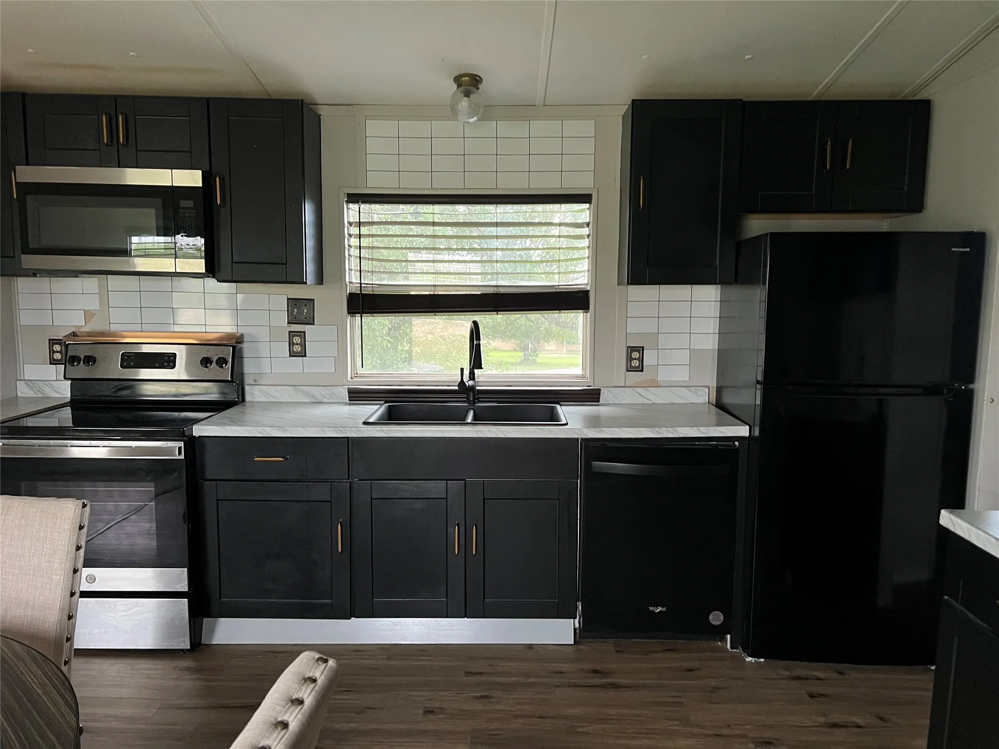 The kitchen features dark cabinetry with gold-toned hardware, a stainless steel microwave and oven, a black dishwasher, and a black refrigerator