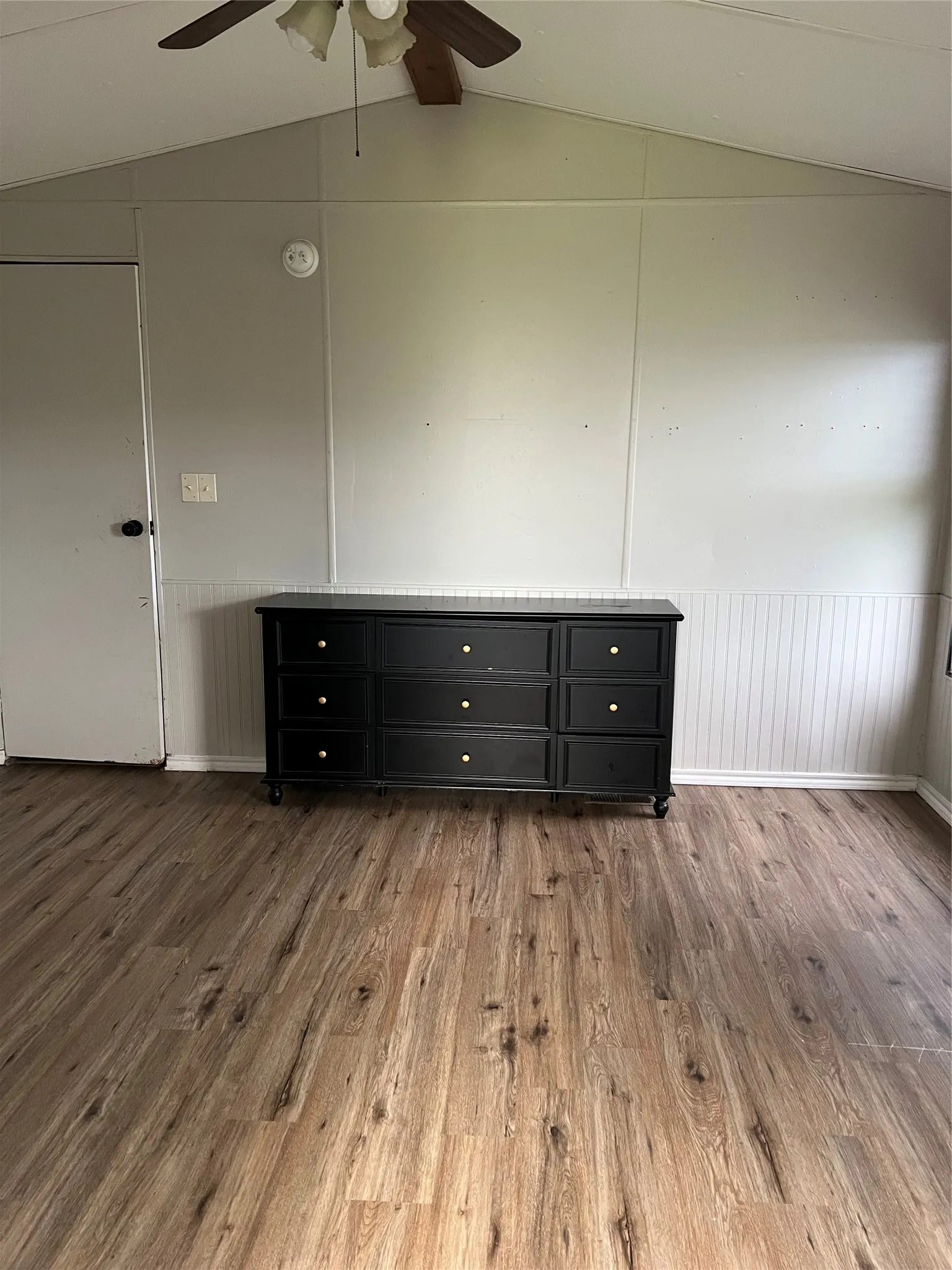 This room features a vaulted ceiling with a ceiling fan, light-colored walls, and wood-look flooring
