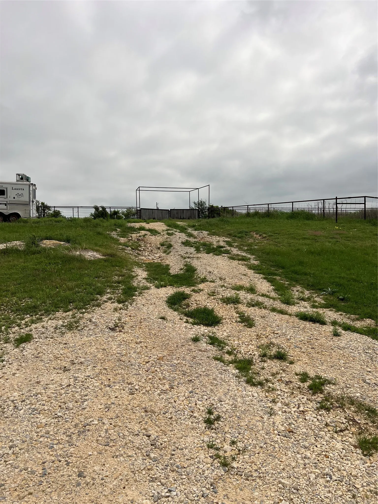 The property features a gravel pathway leading towards a fenced area, bordered by grassy sections