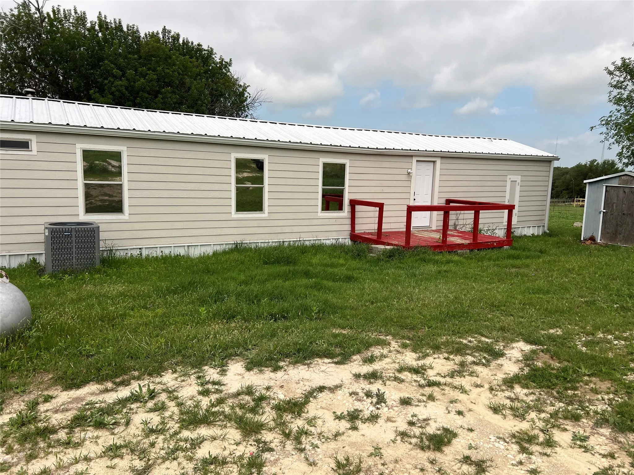 The property features light-colored horizontal siding, a white metal roof, and a red deck