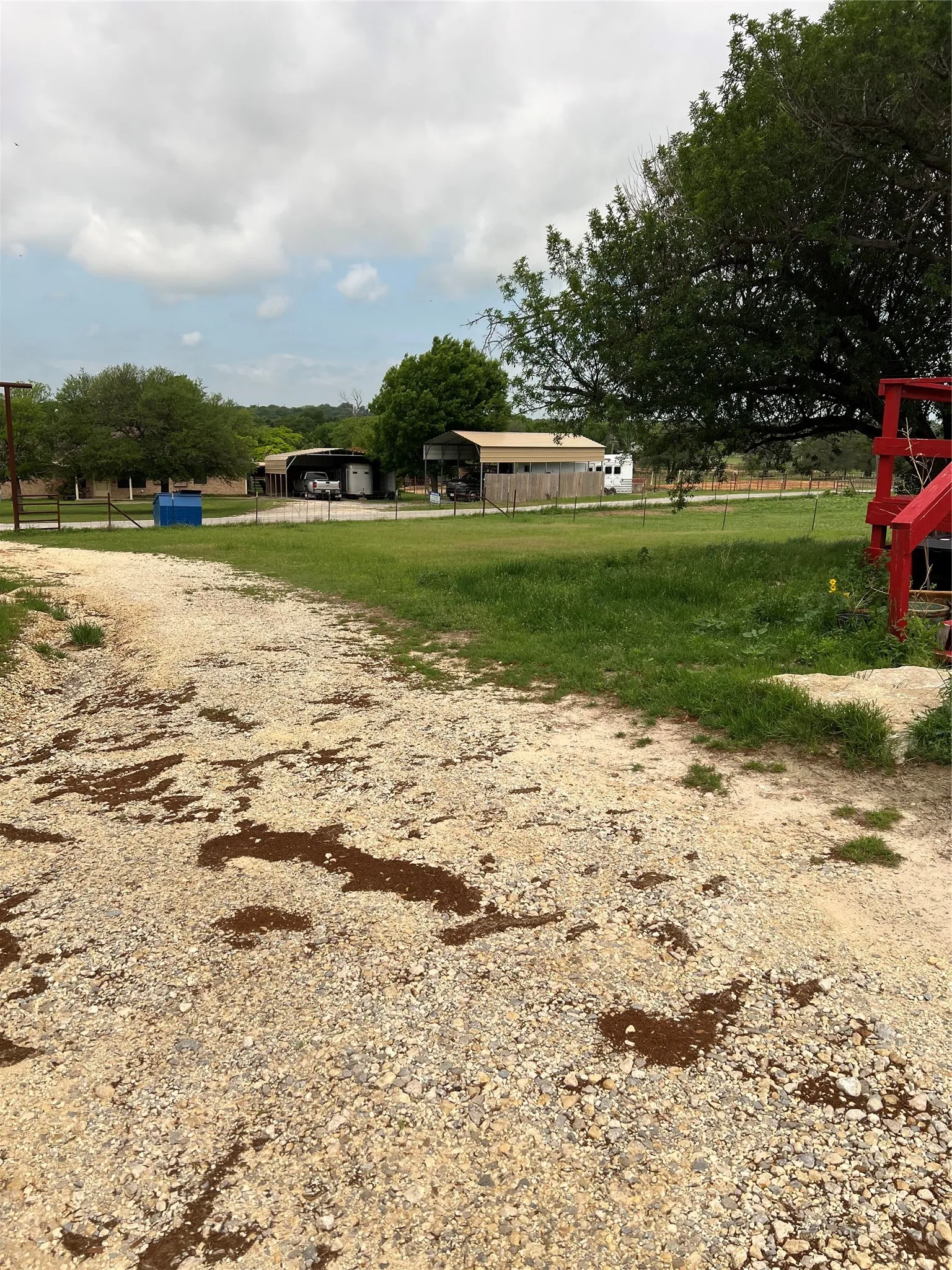 This property features a spacious gravel driveway, expansive green lawns, and several mature trees, providing a natural setting