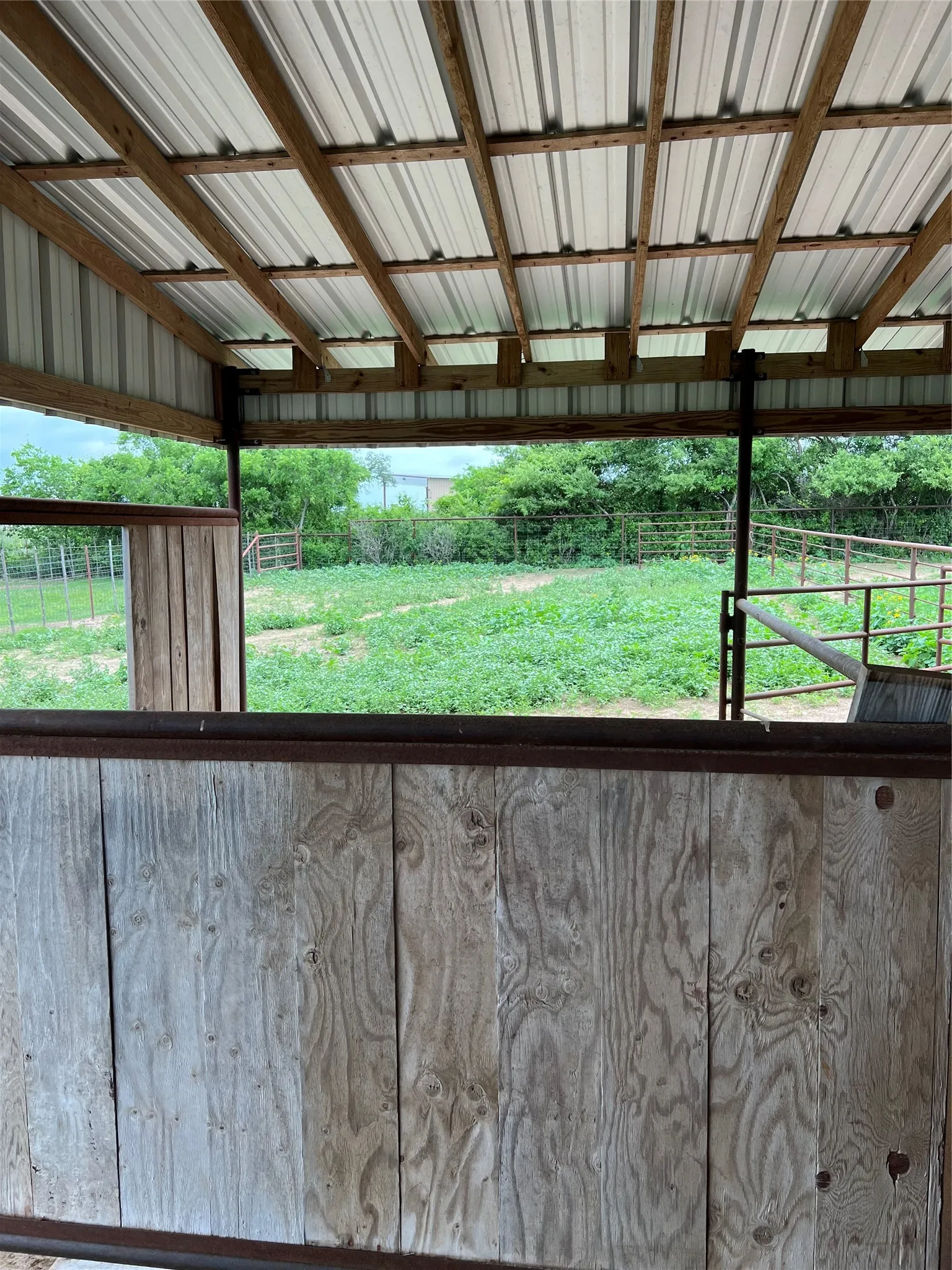 This property features a sturdy wood and metal shelter with a corrugated roof, offering a covered area with open-air views of the expansive green grounds