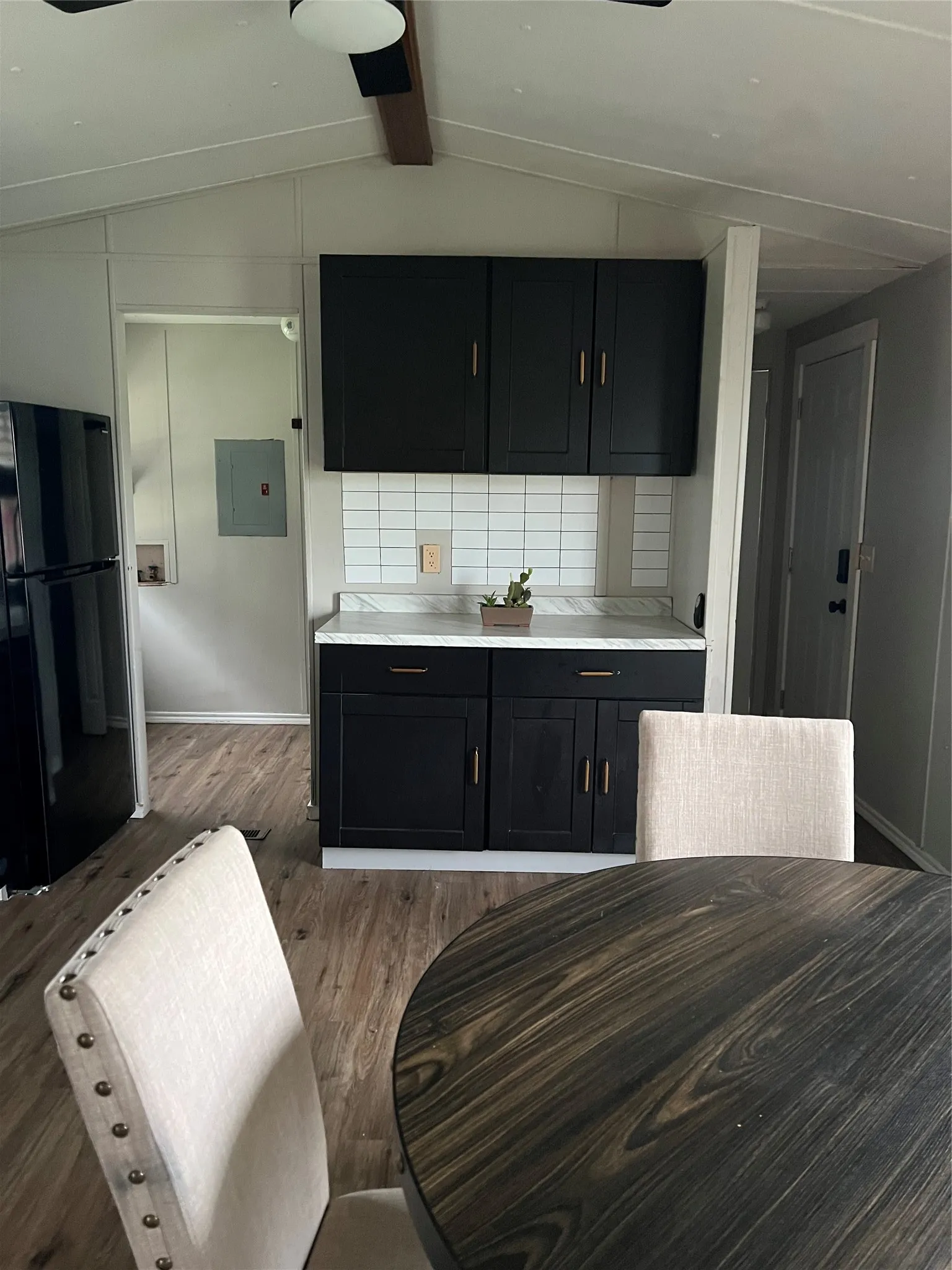 The kitchen features dark cabinetry with gold-toned hardware, a white subway tile backsplash, and a light-colored countertop