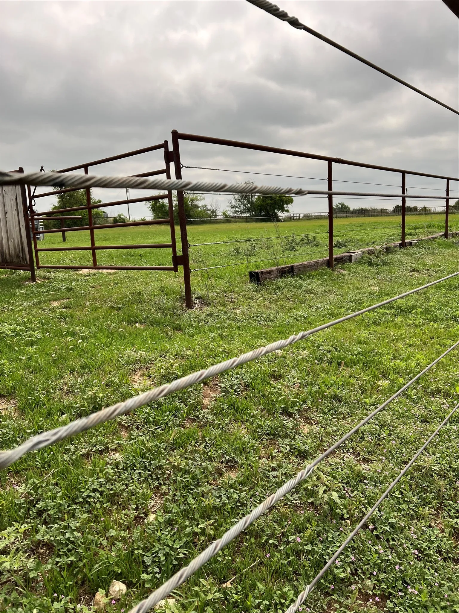 The property features a metal fence and gate, set against a backdrop of open green land