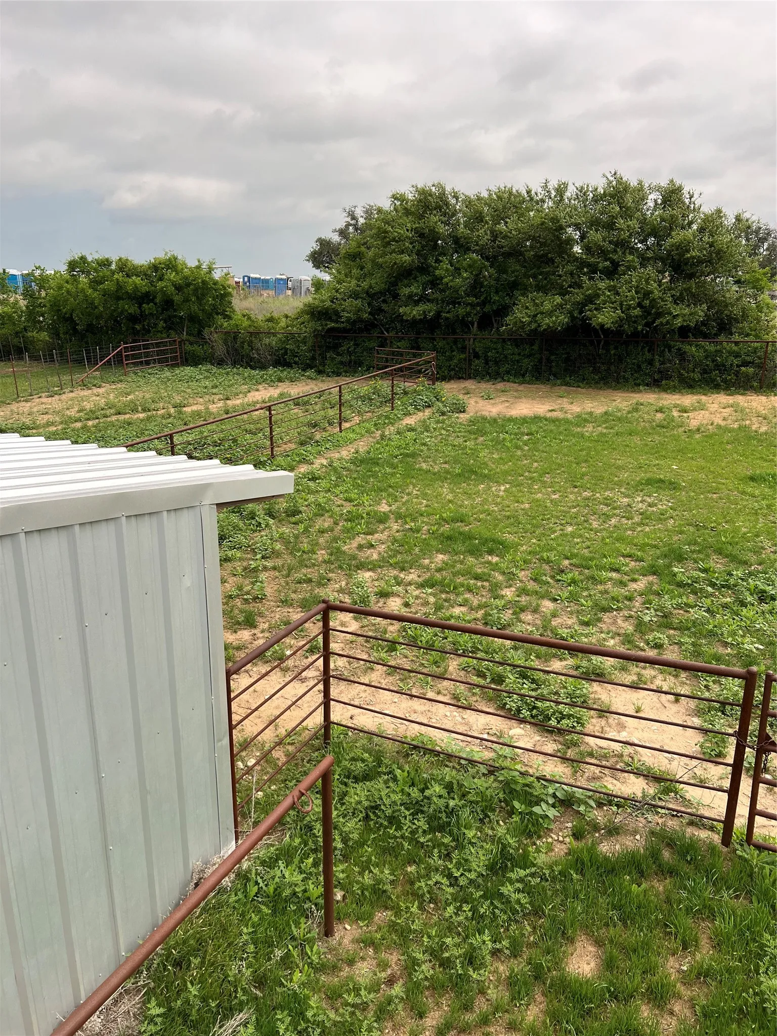 The property features a metal-sided outbuilding, a fence line, and an expanse of green land with mature trees