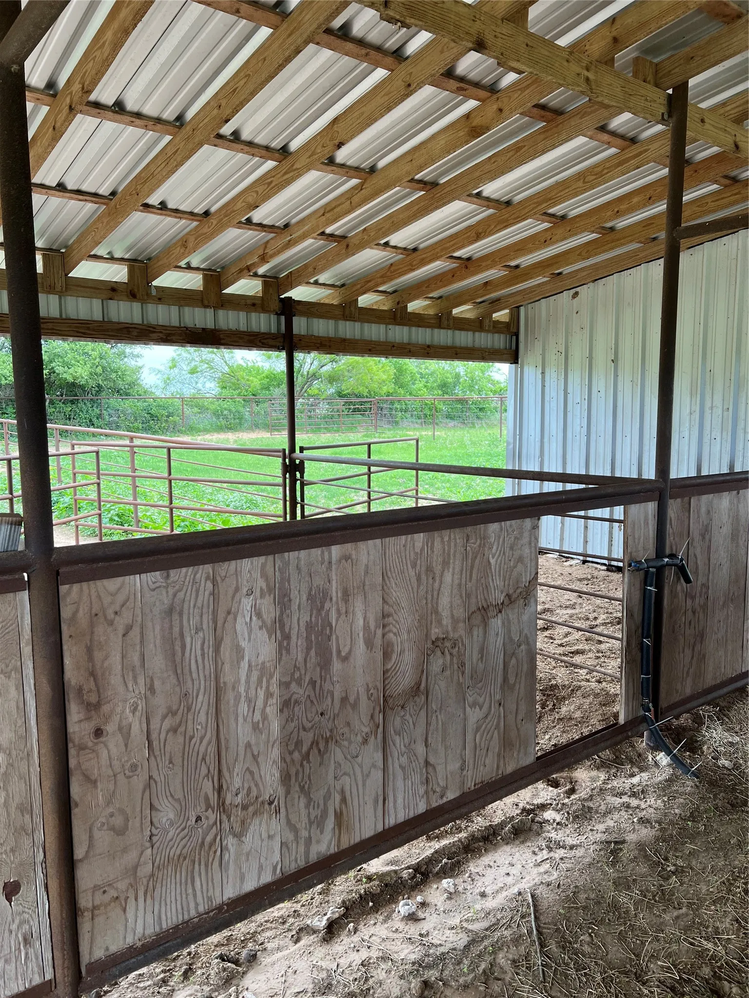 The property features an outdoor structure with a sloped metal roof supported by exposed wood beams, enclosing a section with wood paneling and metal fencing