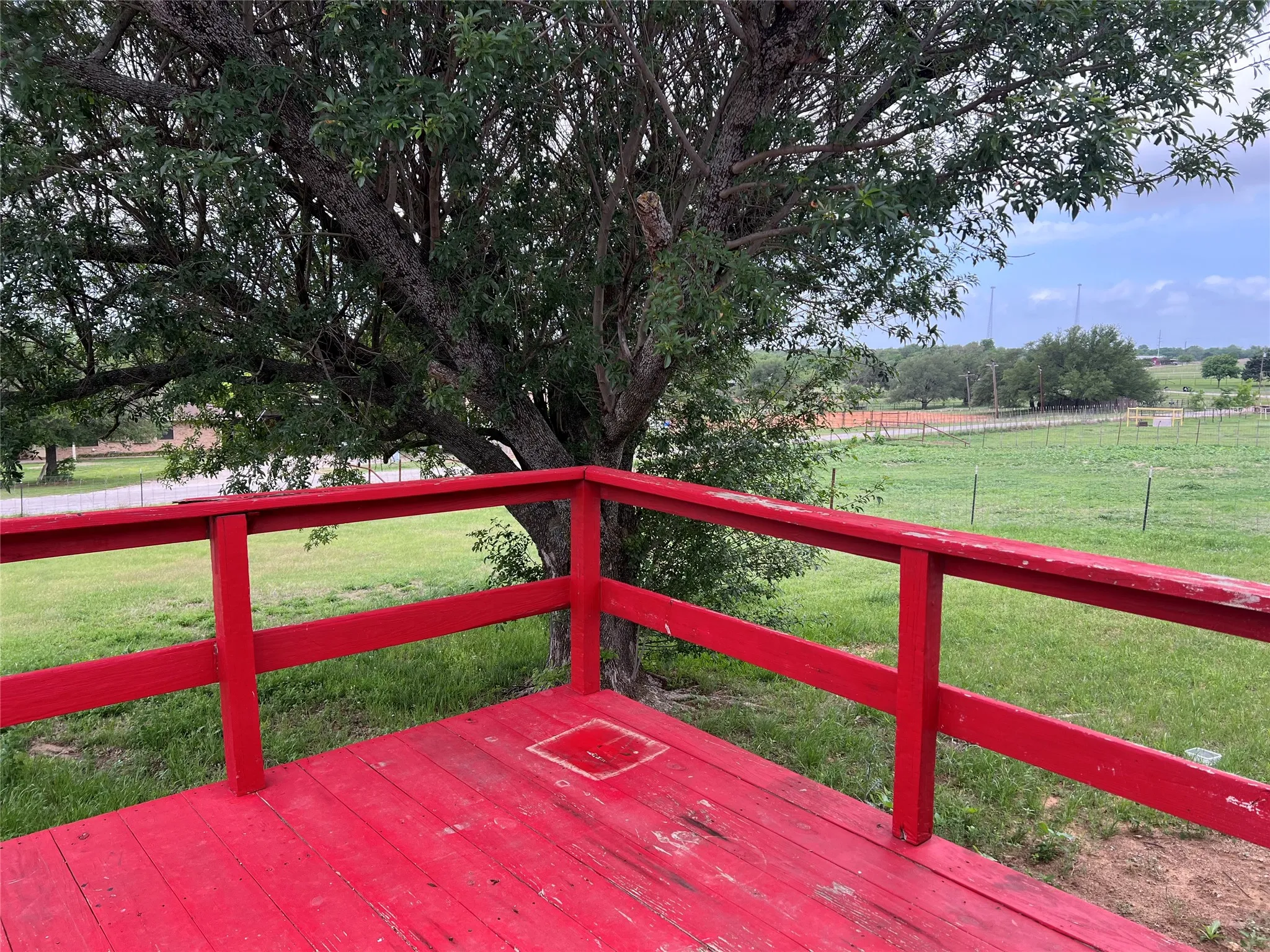 The property features a vibrant red deck with railings, offering views of a grassy area and mature trees