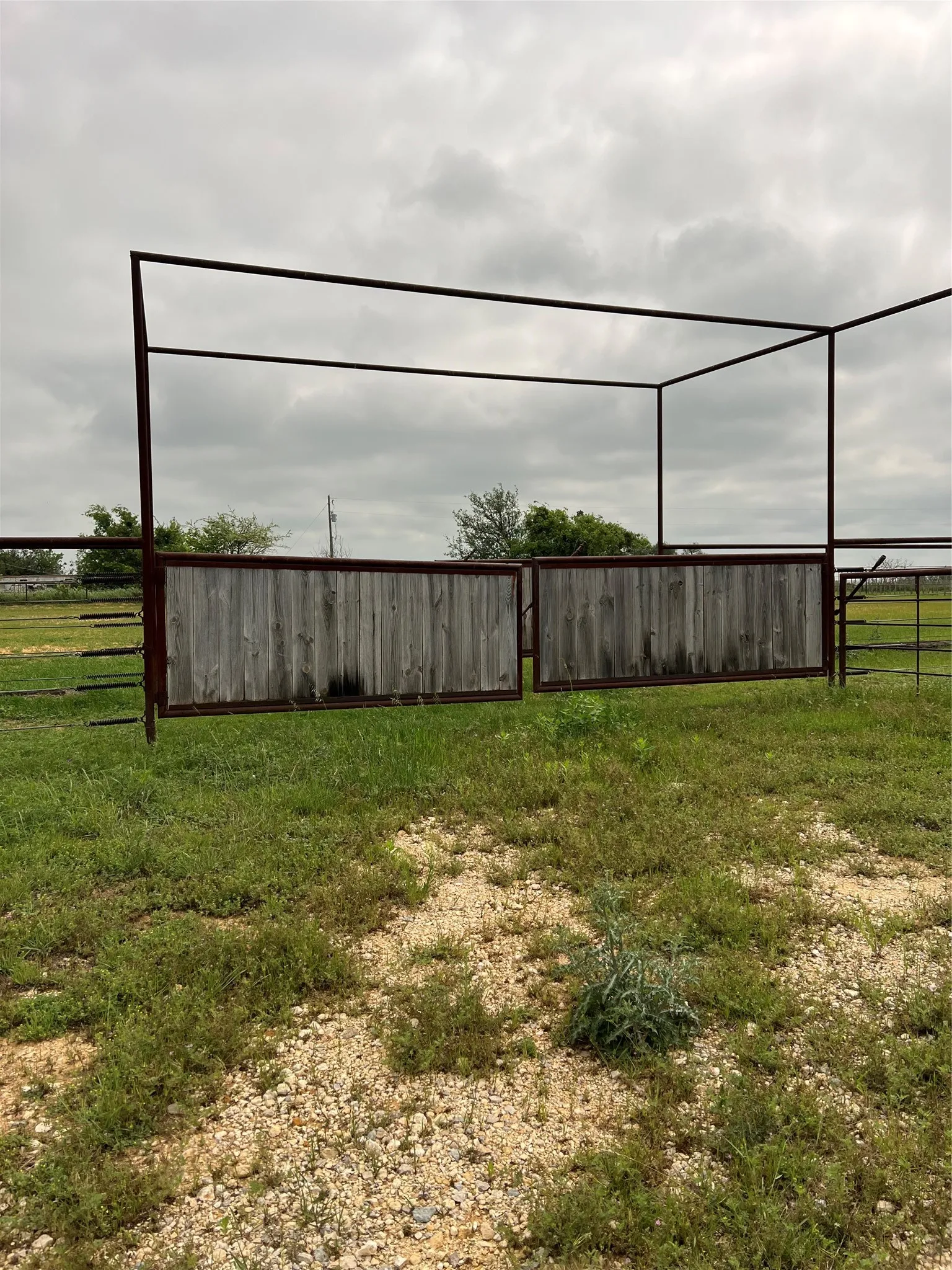 The property features a gated entrance with wooden fencing within a metal frame, surrounded by a grassy area with some gravel