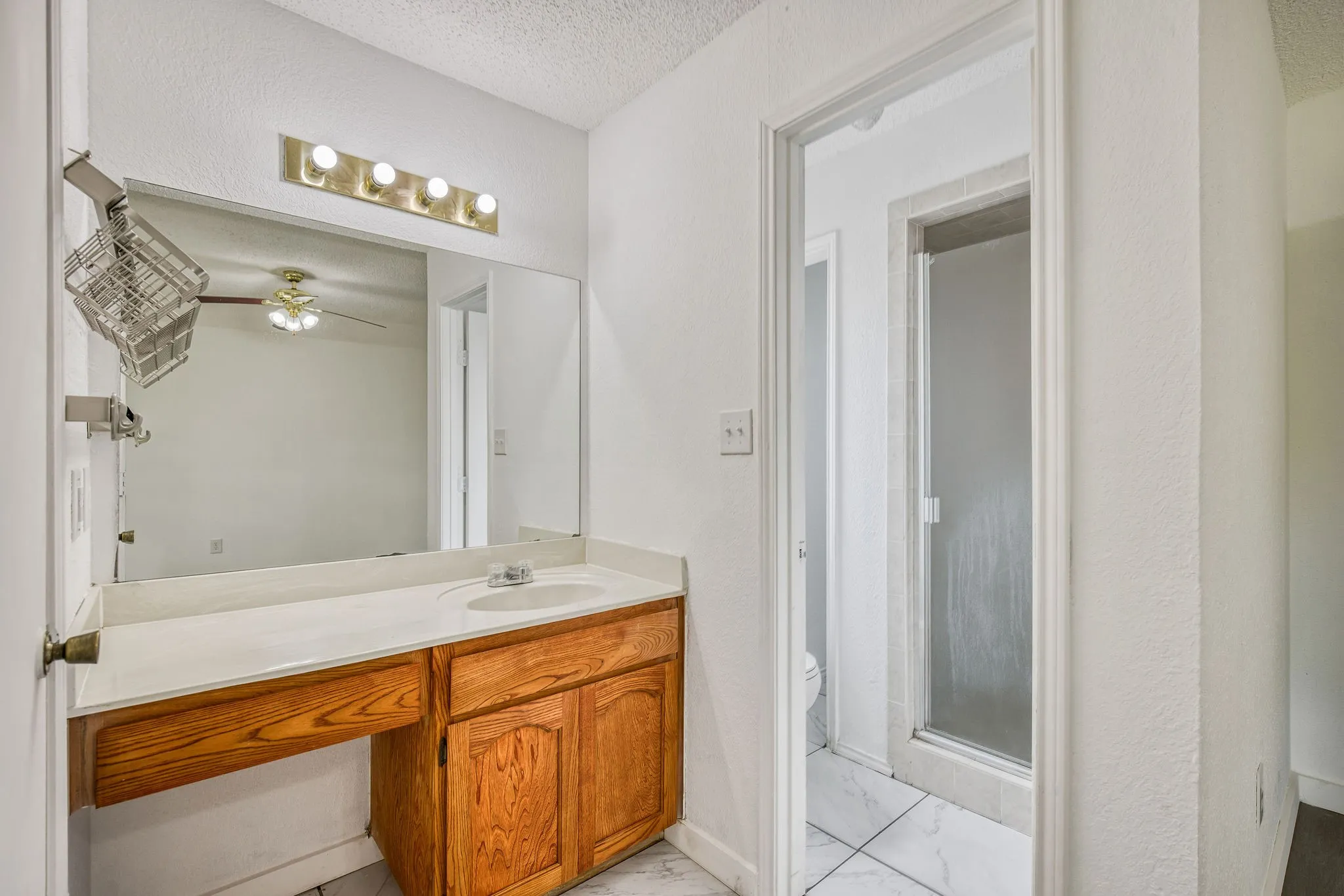 Bathroom vanity with a wood cabinet, a white countertop, and a vanity mirror with overhead lighting