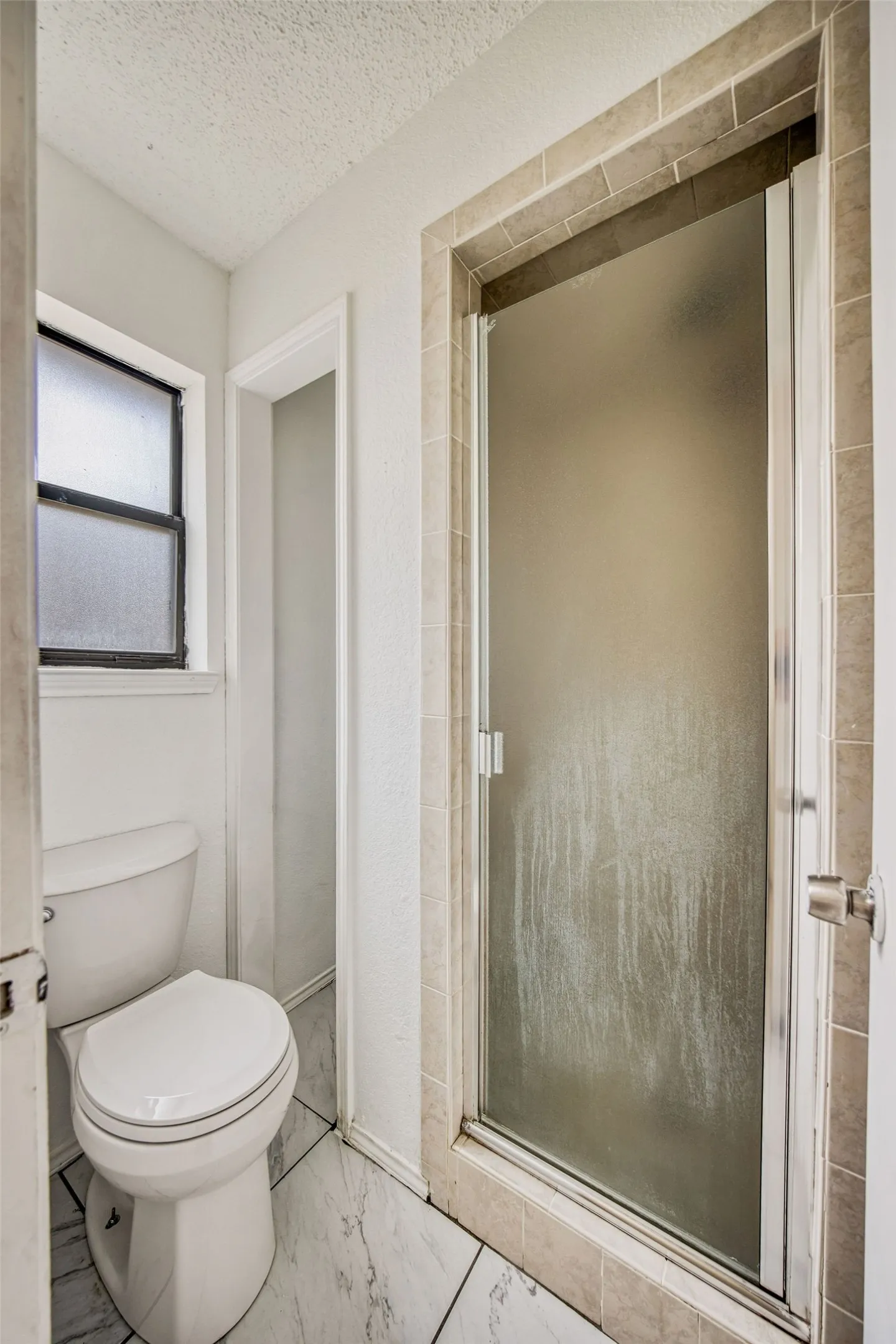 Separate shower with a frosted door for privacy, a toilet, and tiled flooring