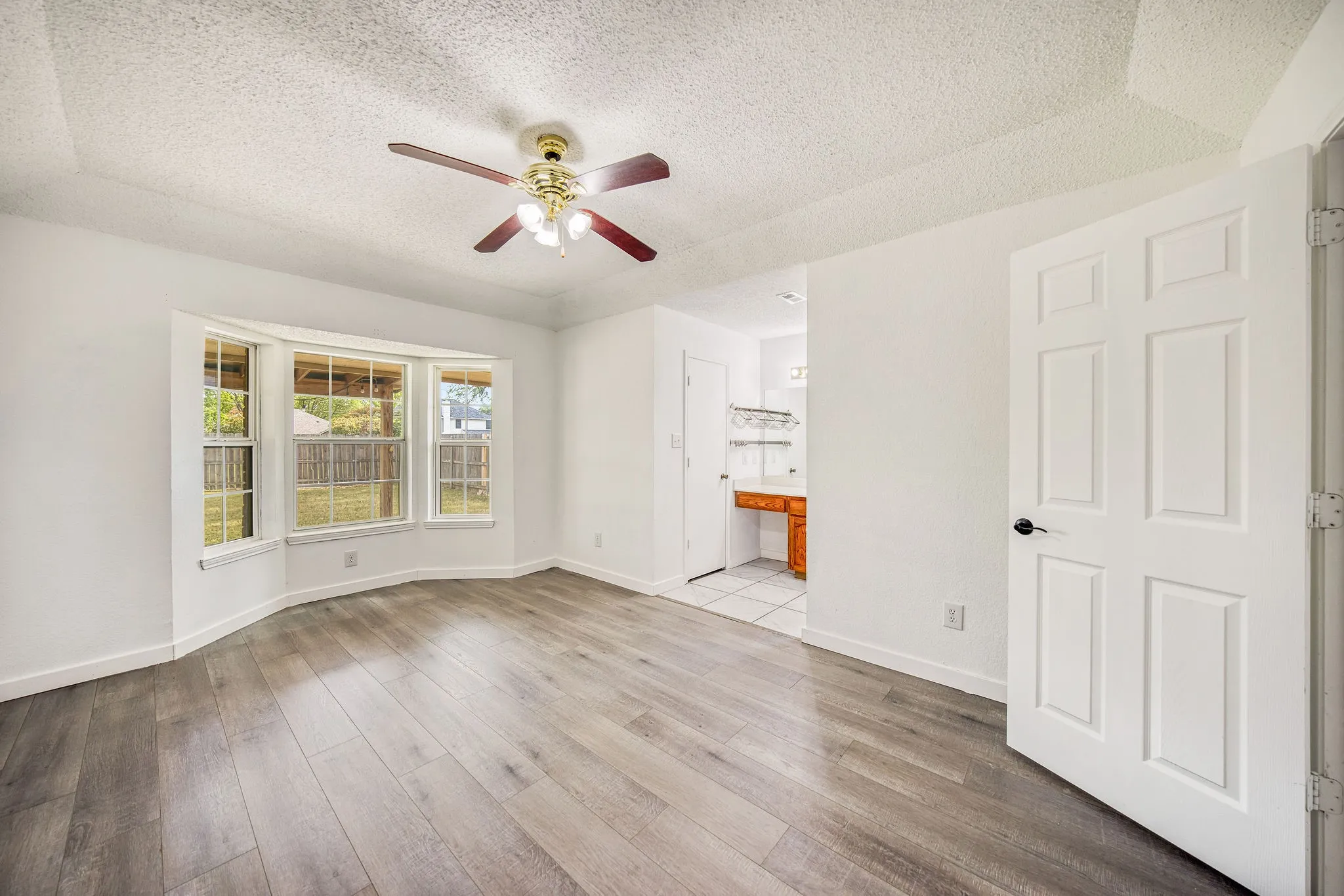 Primary features wood-look flooring, a ceiling fan with integrated lighting, and a bay window providing views of the spacious backyard
