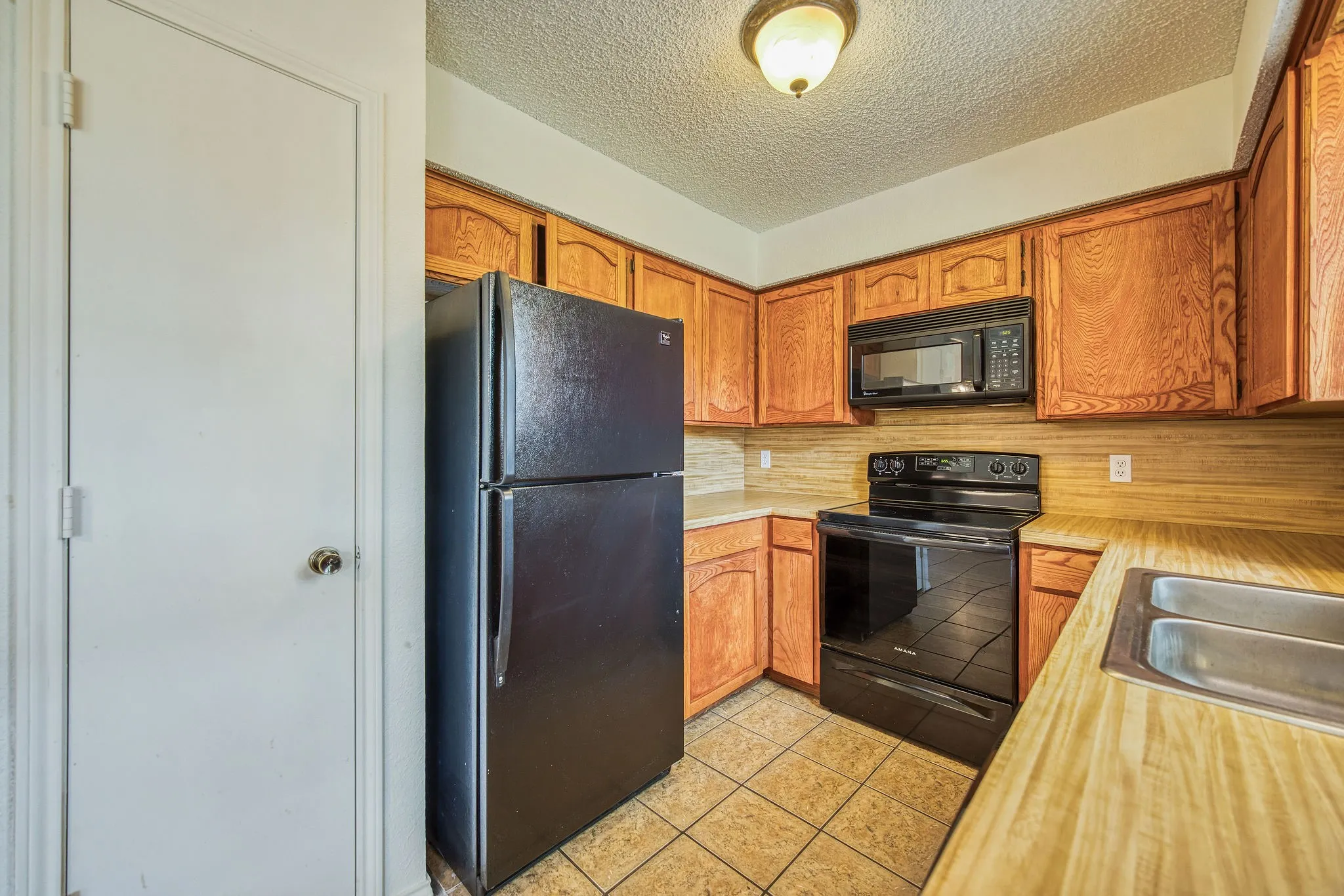 The kitchen features wood cabinetry, a double basin stainless steel sink, black appliances, and tiled flooring