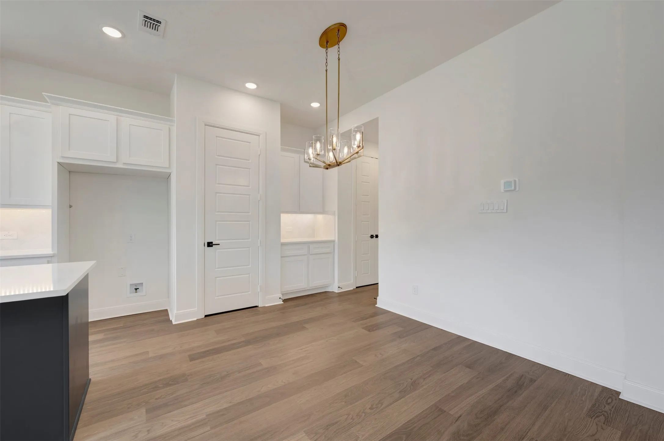 Wood-finish flooring, recessed lighting, white cabinetry, gold-tone chandelier, and a white countertop