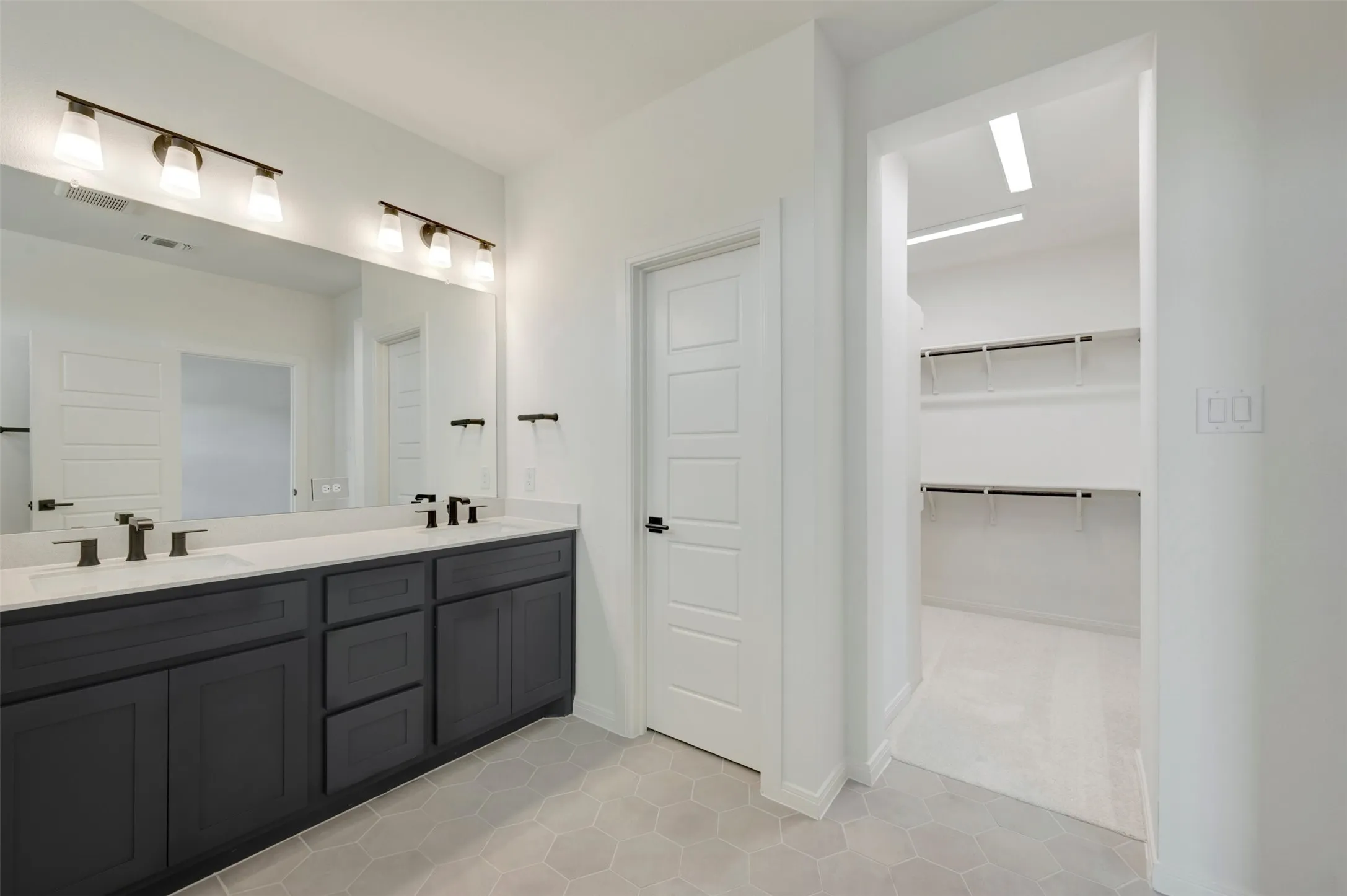 Dual vanity with dark cabinetry and white countertops, large mirror, and adjacent walk-in closet with shelving