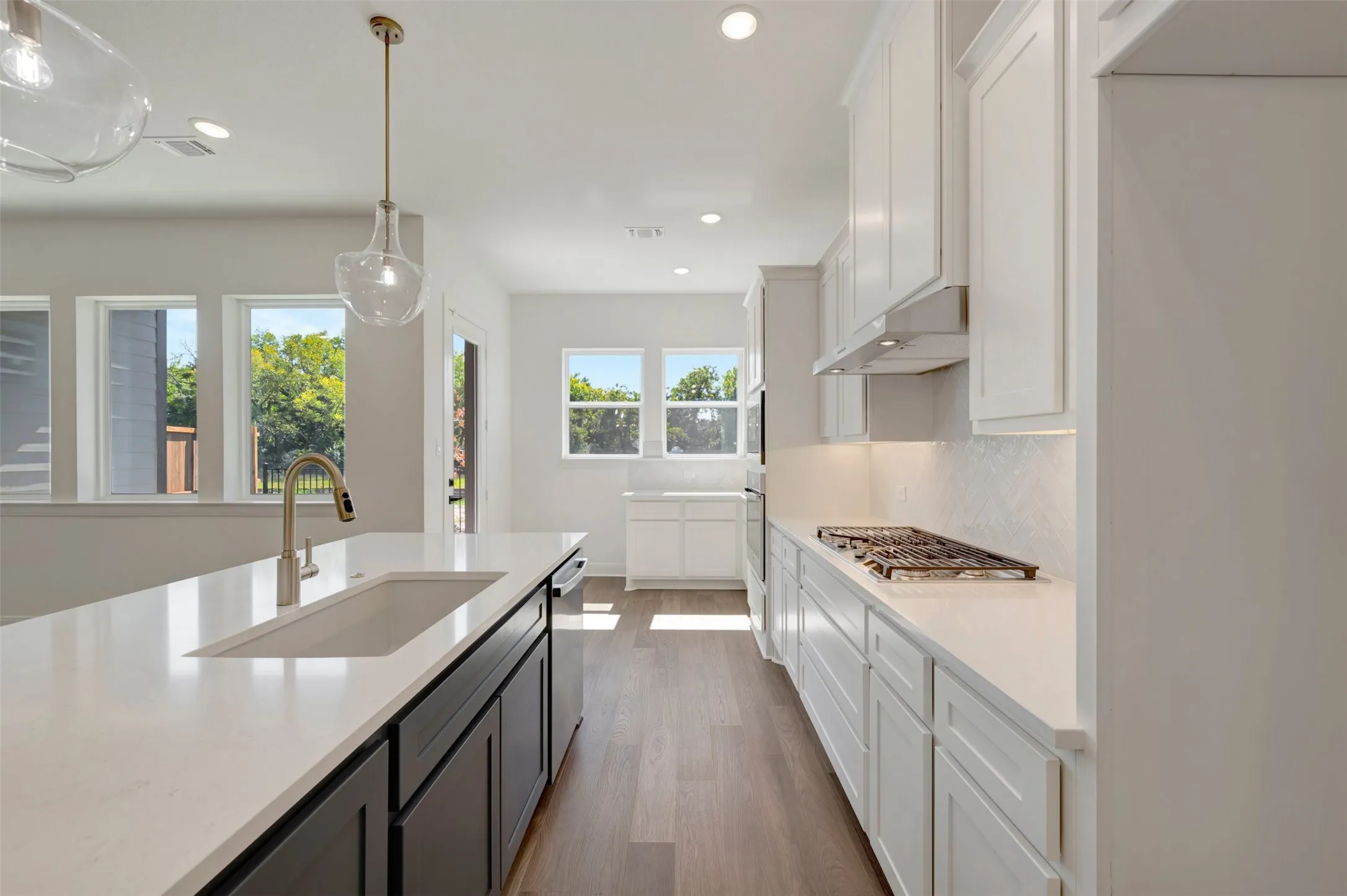 Kitchen featuring an island with an undermount sink, pendant lighting, gas range, white cabinetry, and wood-finish flooring