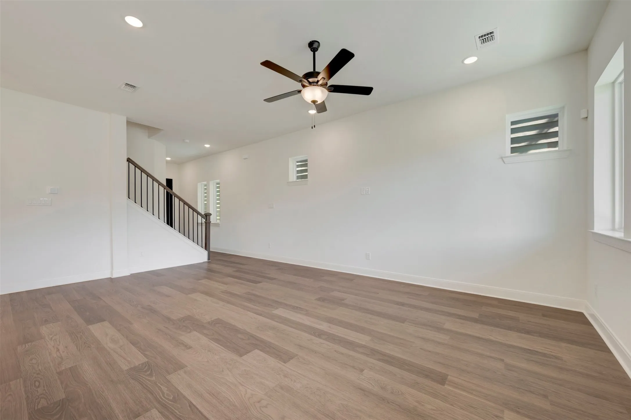 Spacious room featuring wood-finish flooring, recessed lighting, a ceiling fan, and multiple windows