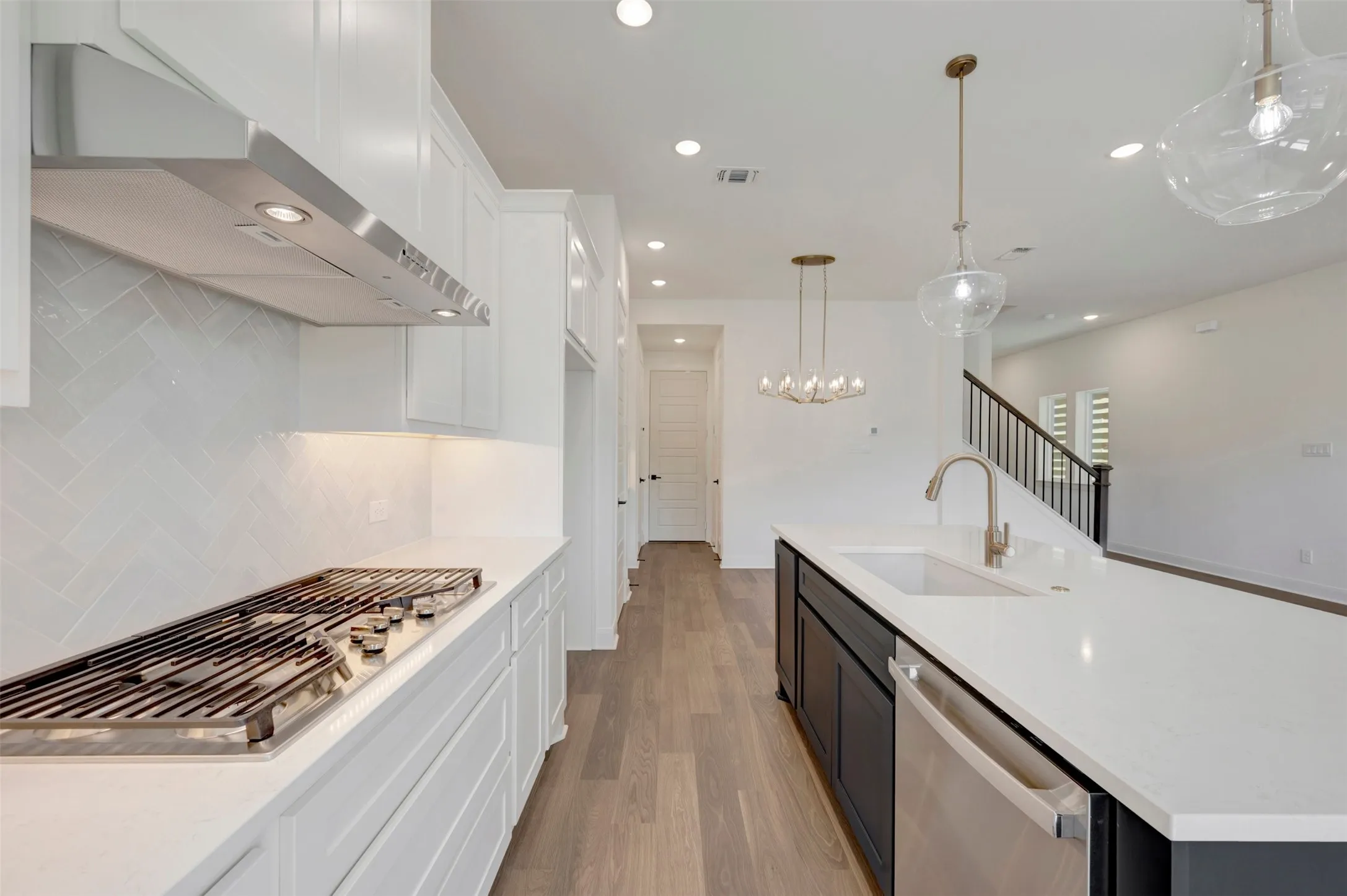 White cabinetry with under-cabinet lighting, herringbone tile backsplash, stainless steel gas cooktop, center island with an undermount sink, and wood-finish flooring
