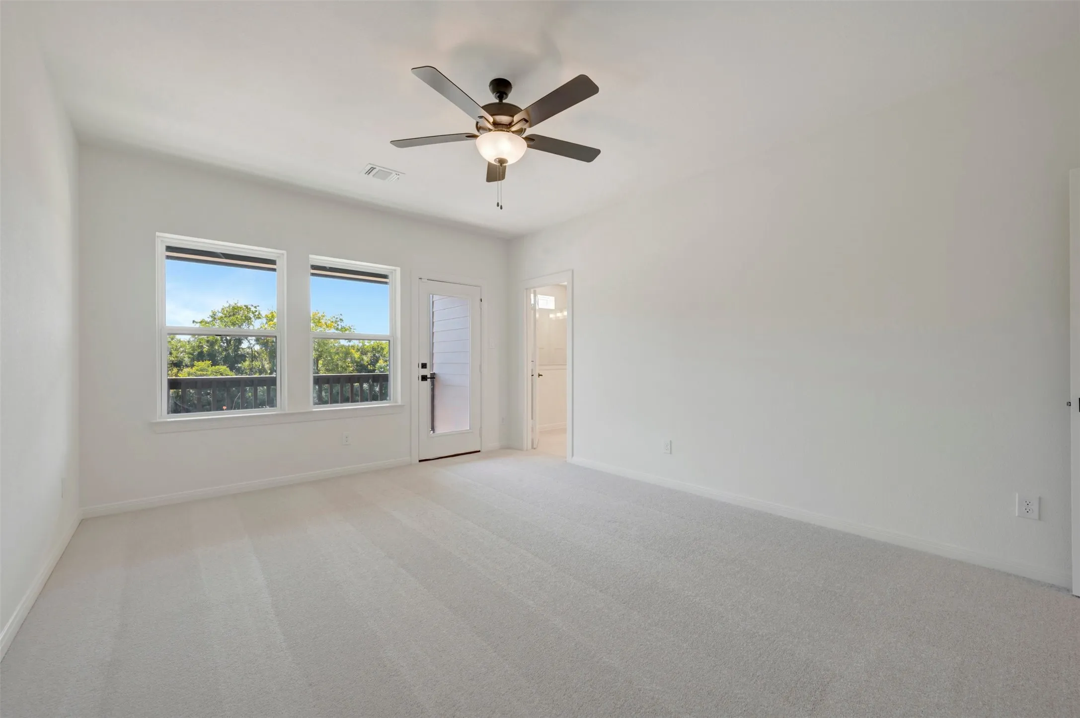 Spacious interior with neutral carpeting, two large windows, and a glass-paneled door