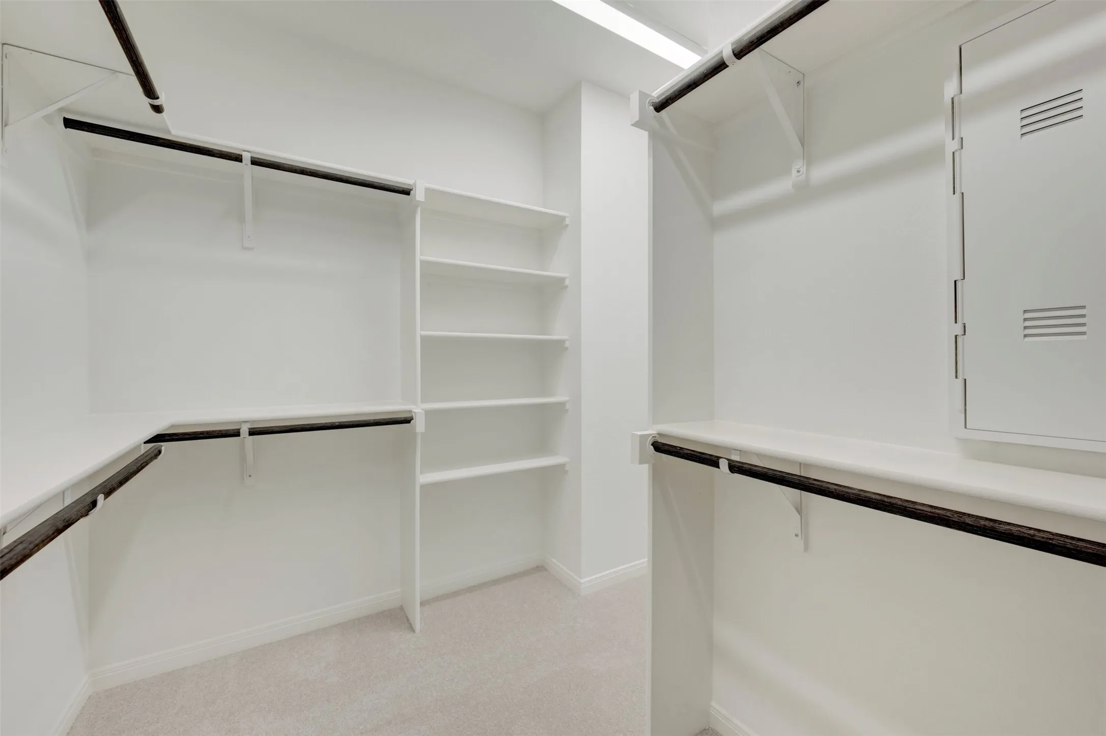 Built-in shelving, white walls, black garment rods, carpet flooring, and recessed lighting