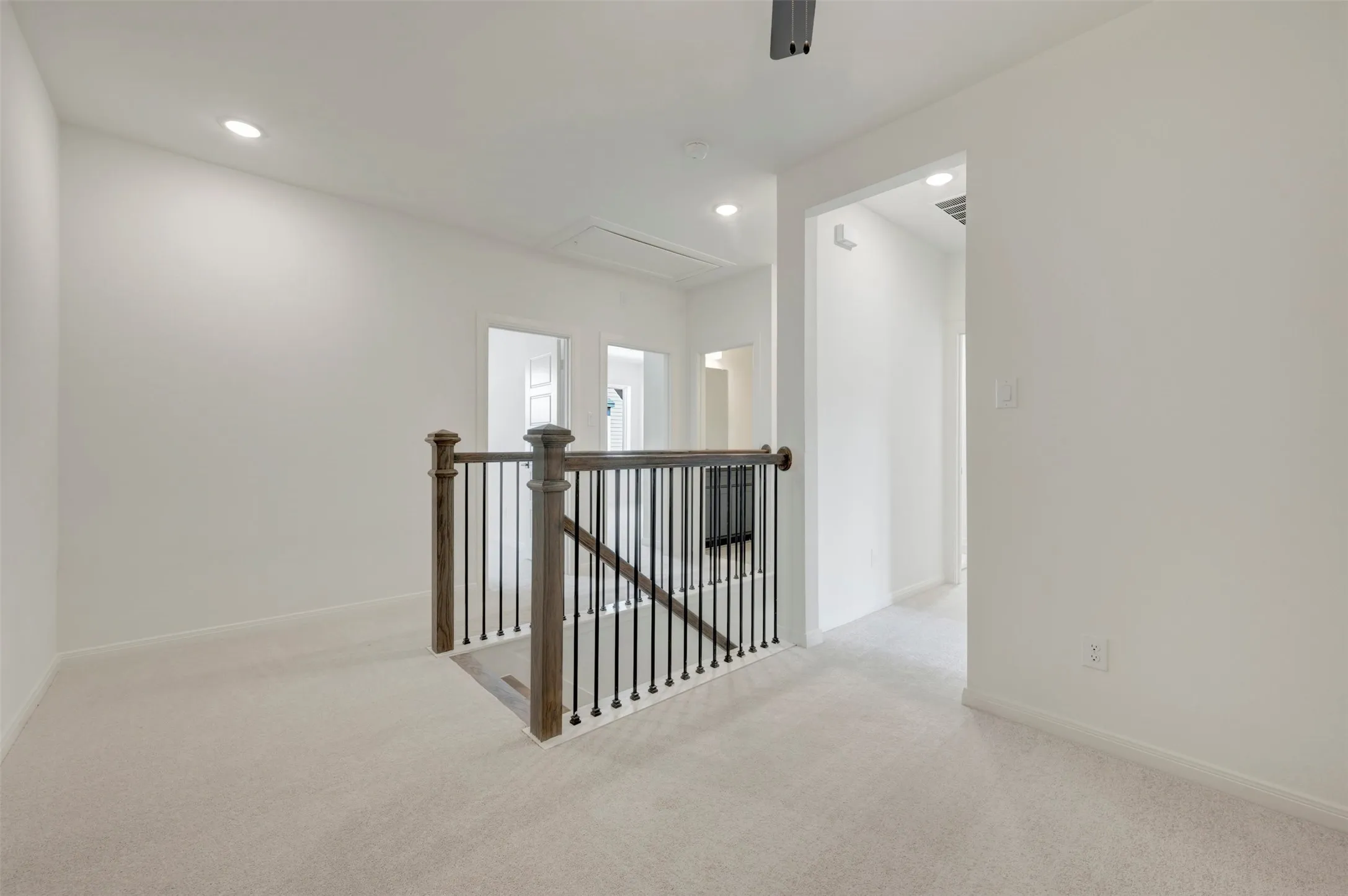 Carpeted landing featuring recessed lighting, a dark wood-finish newel post, and black wrought iron balusters