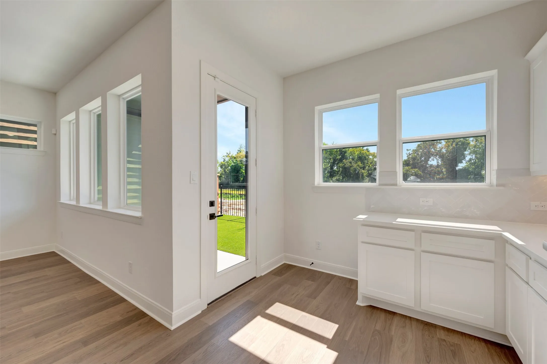 Wood-finish flooring throughout, multiple windows, built-in white cabinetry, white countertops, and a full-light door providing access to the exterior