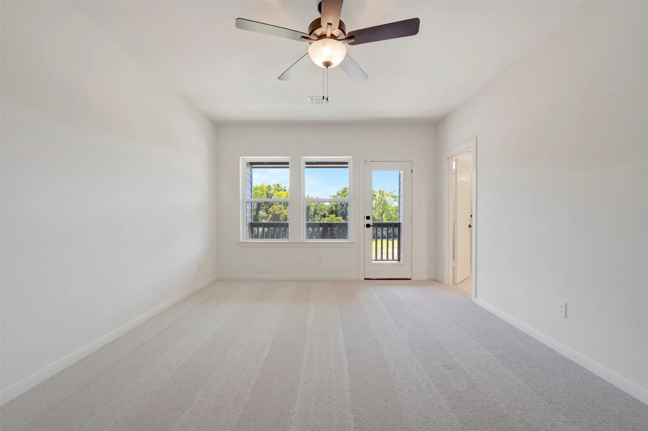 Light-toned carpeting, white walls, three windows with black frames, and a glass-paneled door