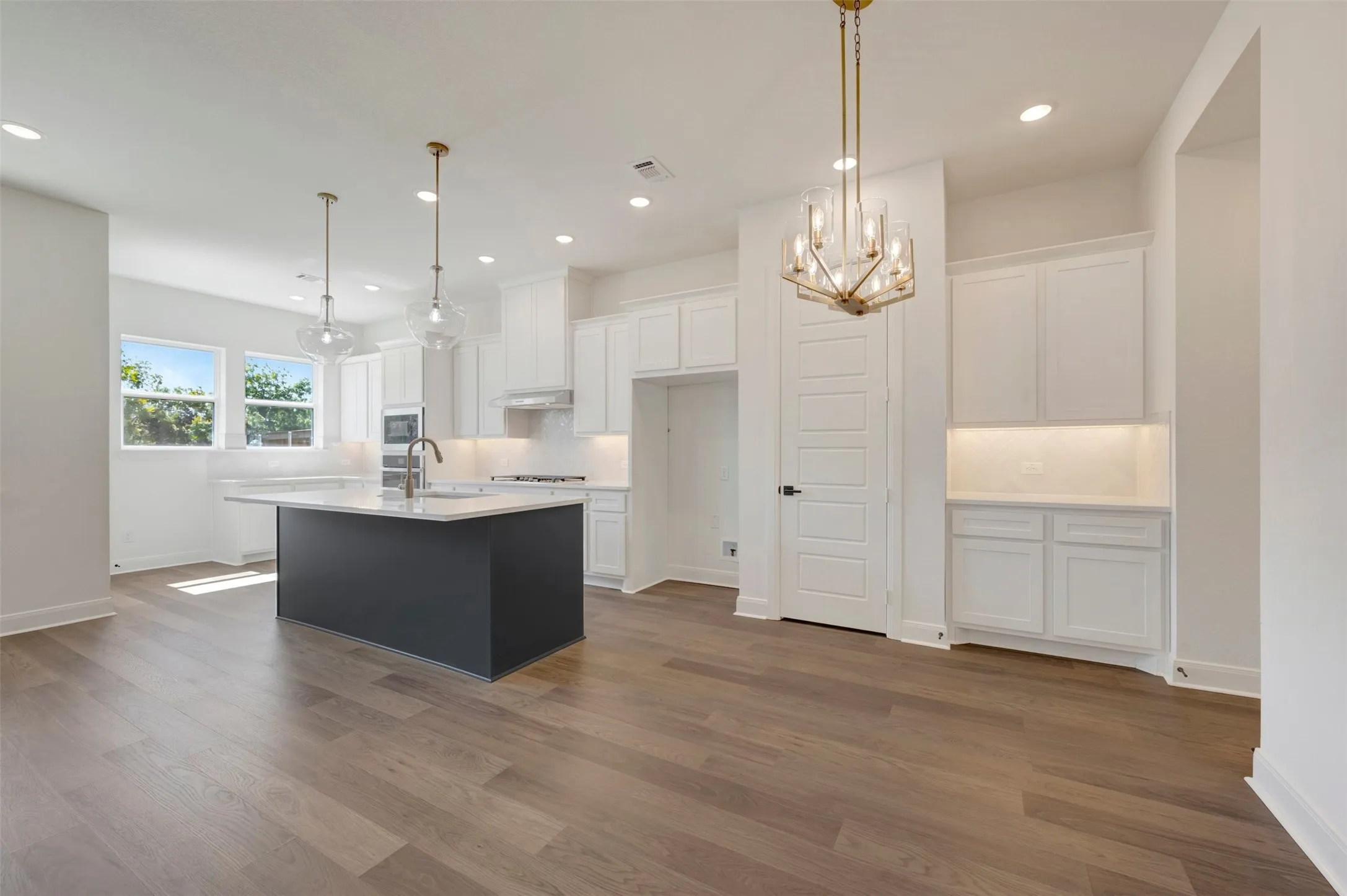Kitchen featuring a contrasting island with seating, pendant lighting, built-in cabinetry, and wood-finish flooring