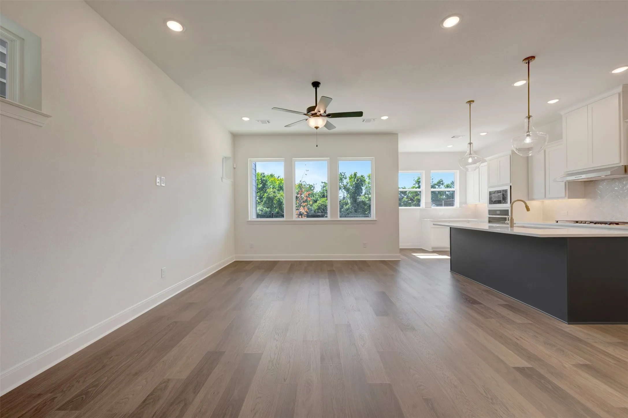 Wood-finish flooring throughout, recessed lighting, ceiling fan, multiple windows with natural light, and a kitchen island with pendant lighting
